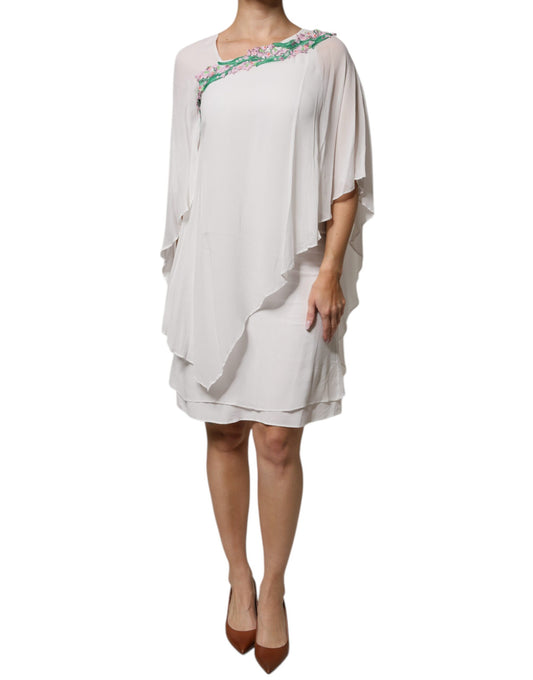 A woman wearing a white floral embroidered chiffon shift dress with long sleeves