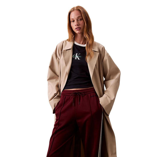 Woman wearing a tan trench coat over maroon pants