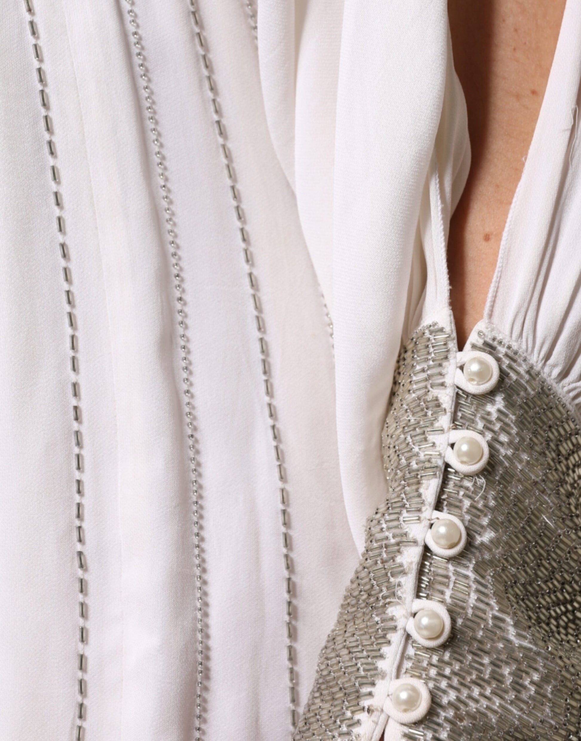 A long white dress with embellishments, featuring a pearl button closure and a sheer overlay