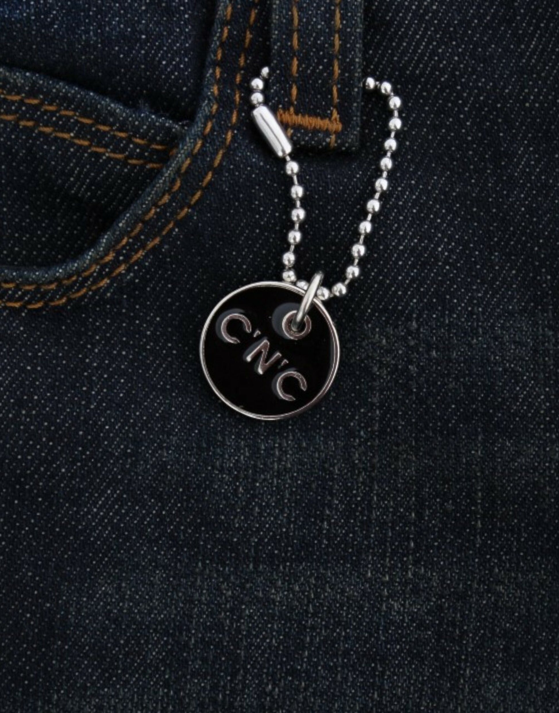 Silver necklace with a round pendant featuring the letters CNC in black
