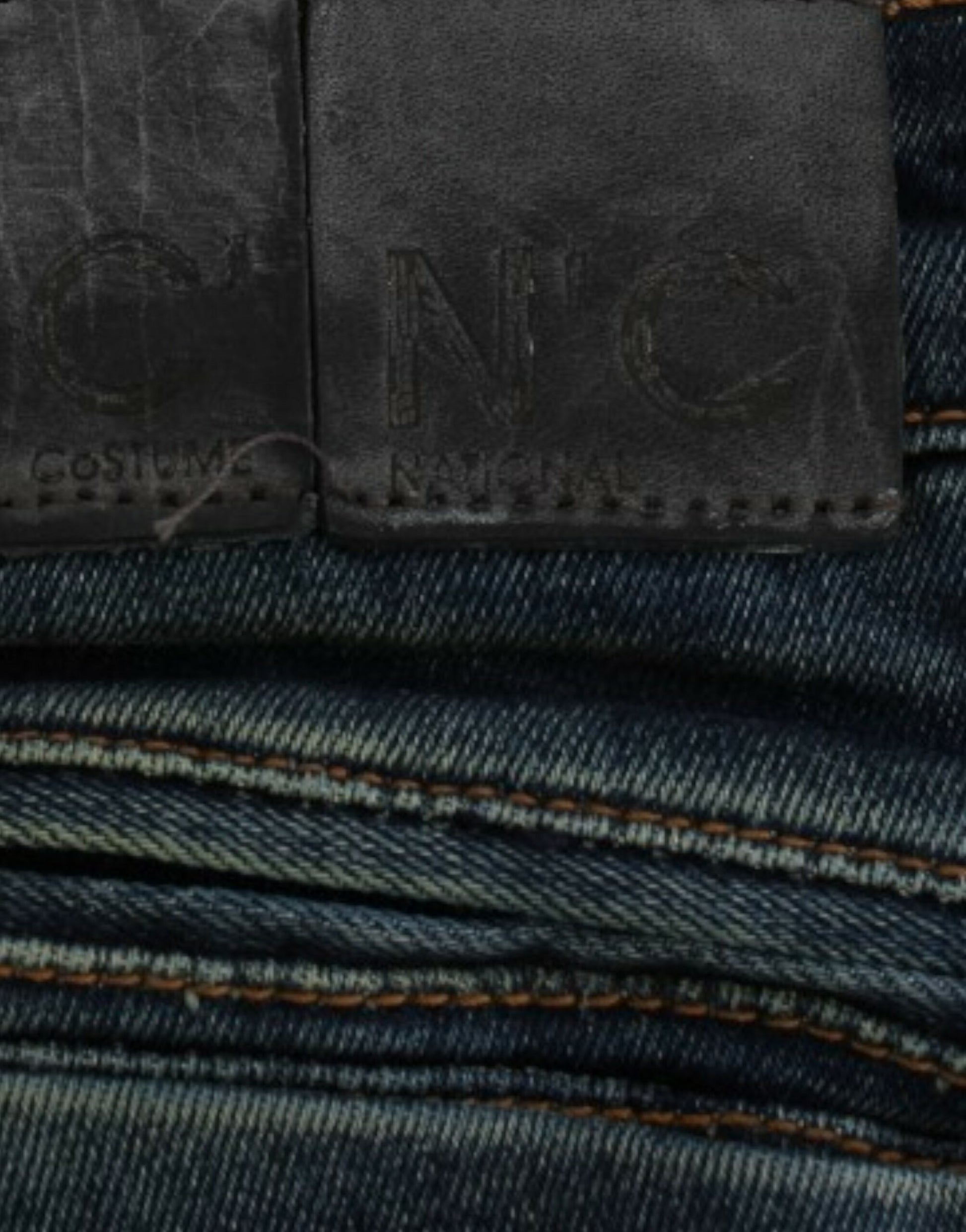 A pair of jeans with visible stitching and a leather patch on the waistband. The patch has embossed letters that are not