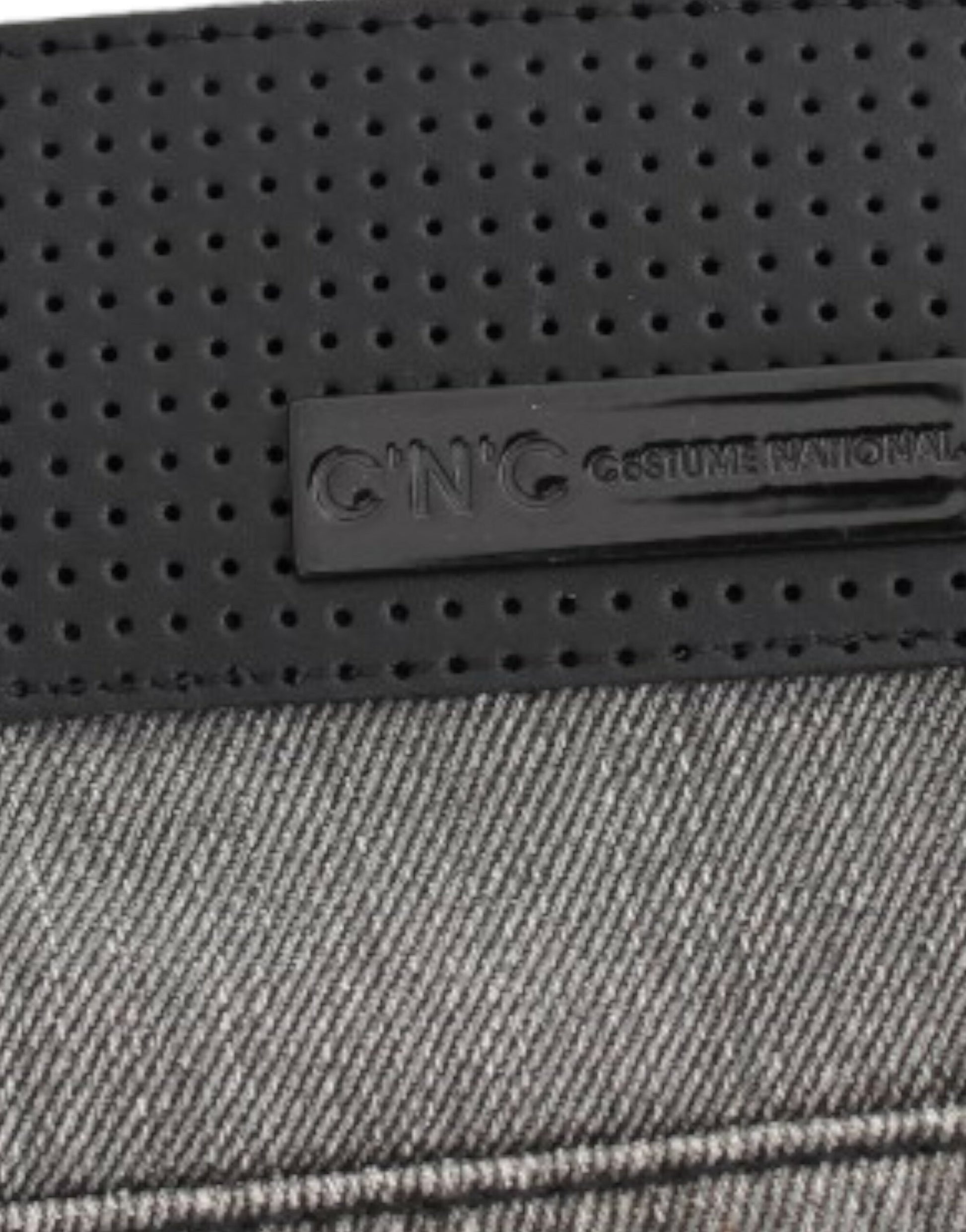 A close-up of a fabric with a visible brand label that reads CNG COSTUME NATIONAL. The fabric appears to be denim or a si
