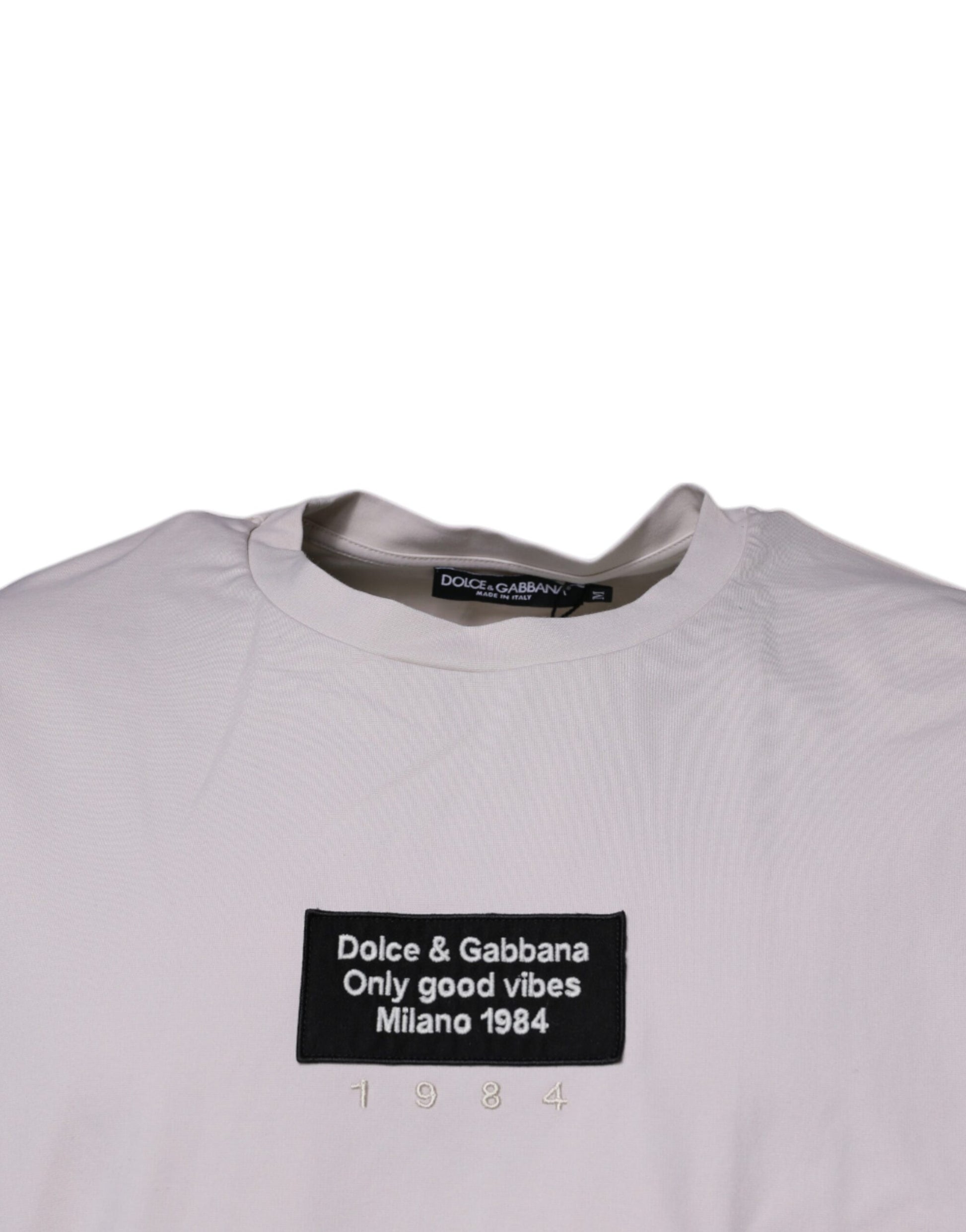 The shirt is beige with a black logo on the front