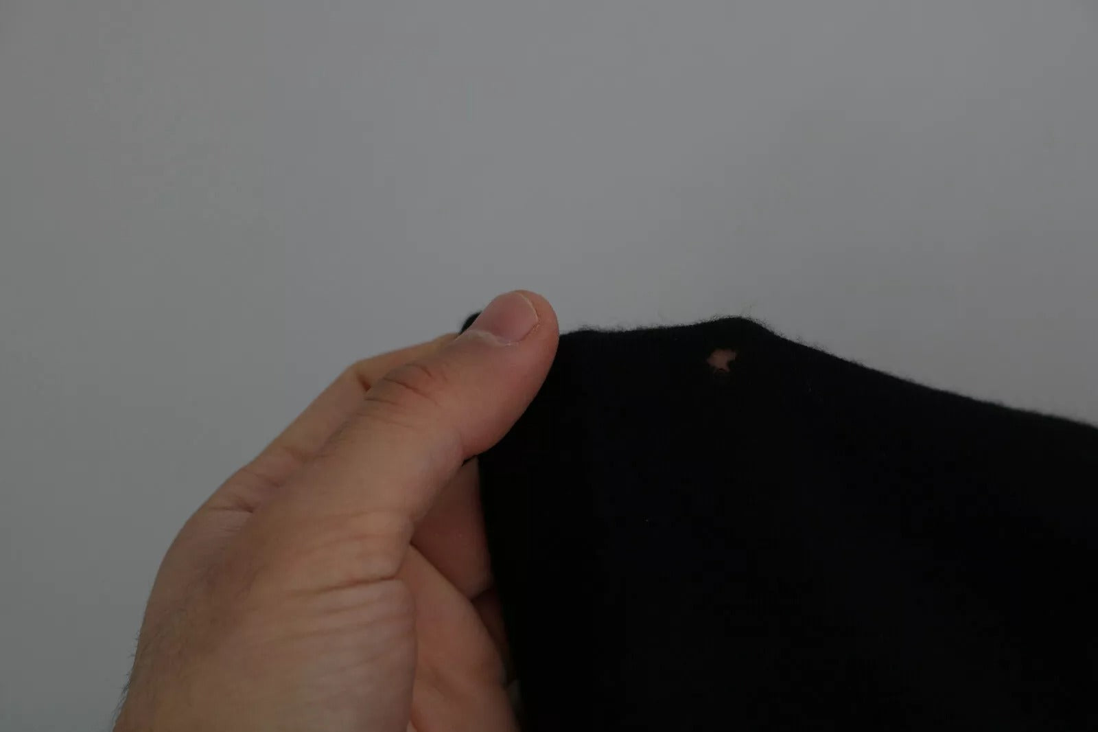 Hand holding black fabric with hole in seam