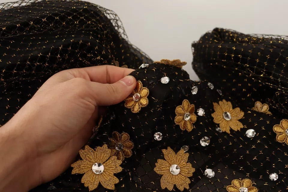 A person is sewing gold flowers onto a black dress with crystals