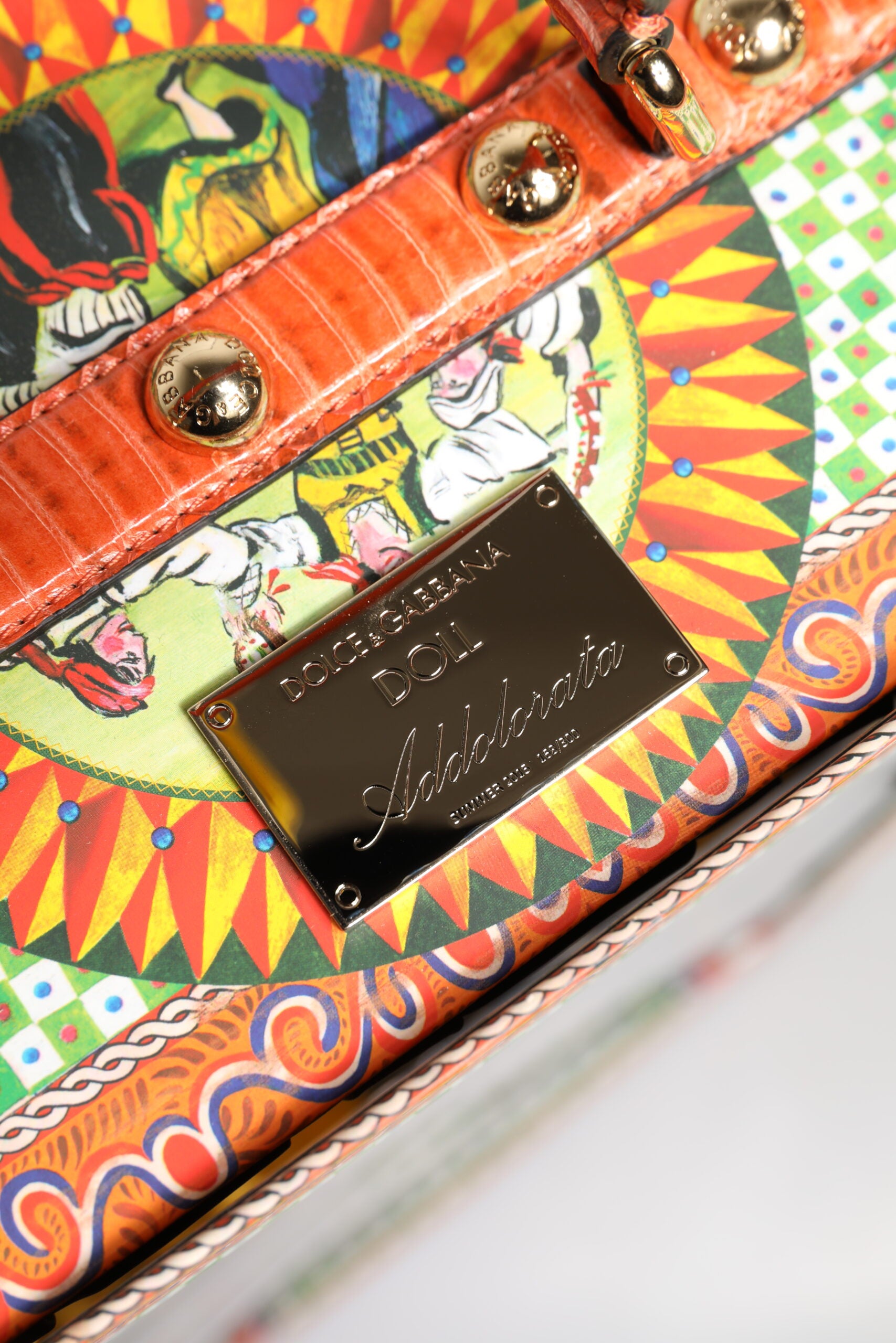 A black leather handbag with a gold buckle and a ceramic plaque on the front