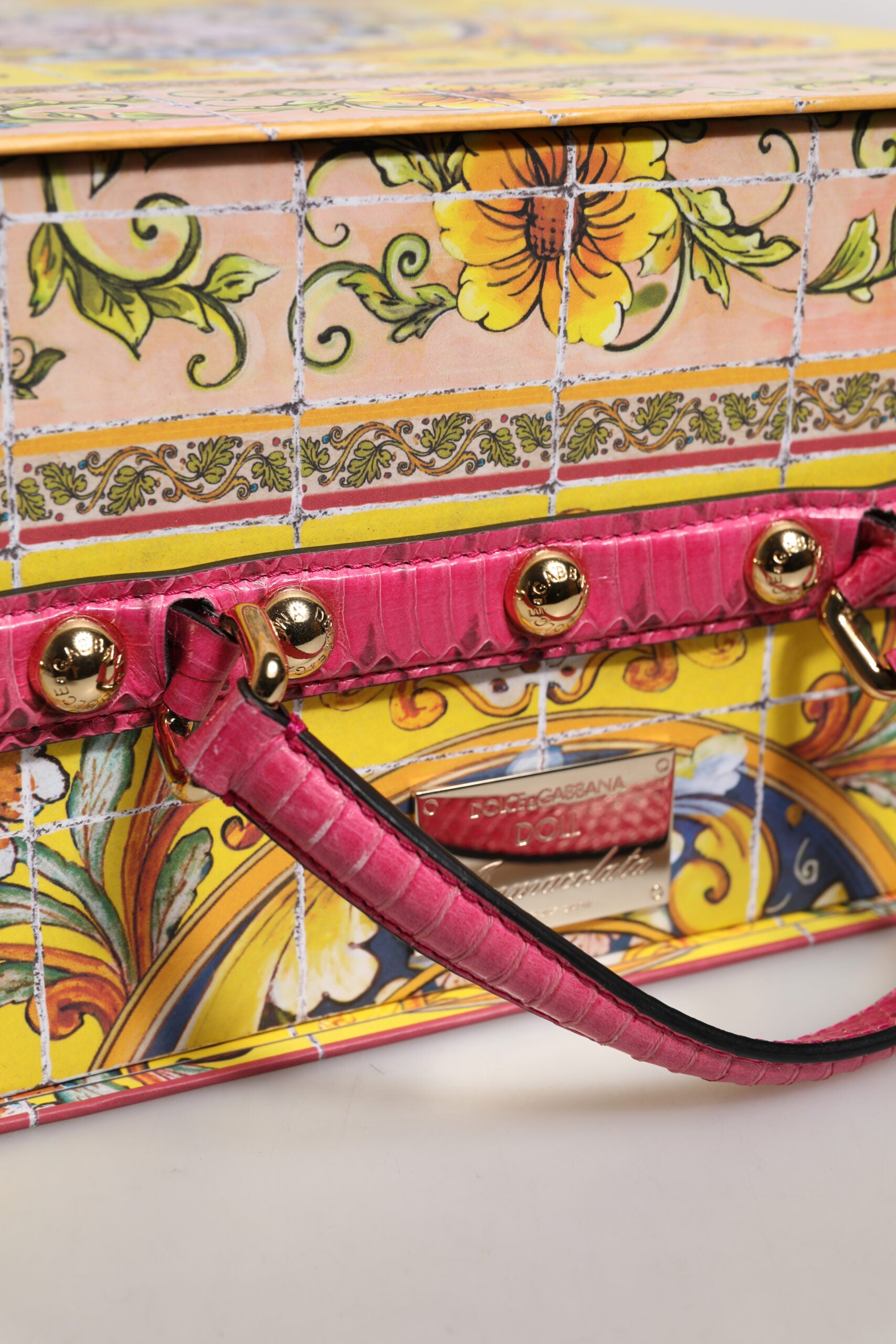 A pink leather handbag with gold accents and a floral design