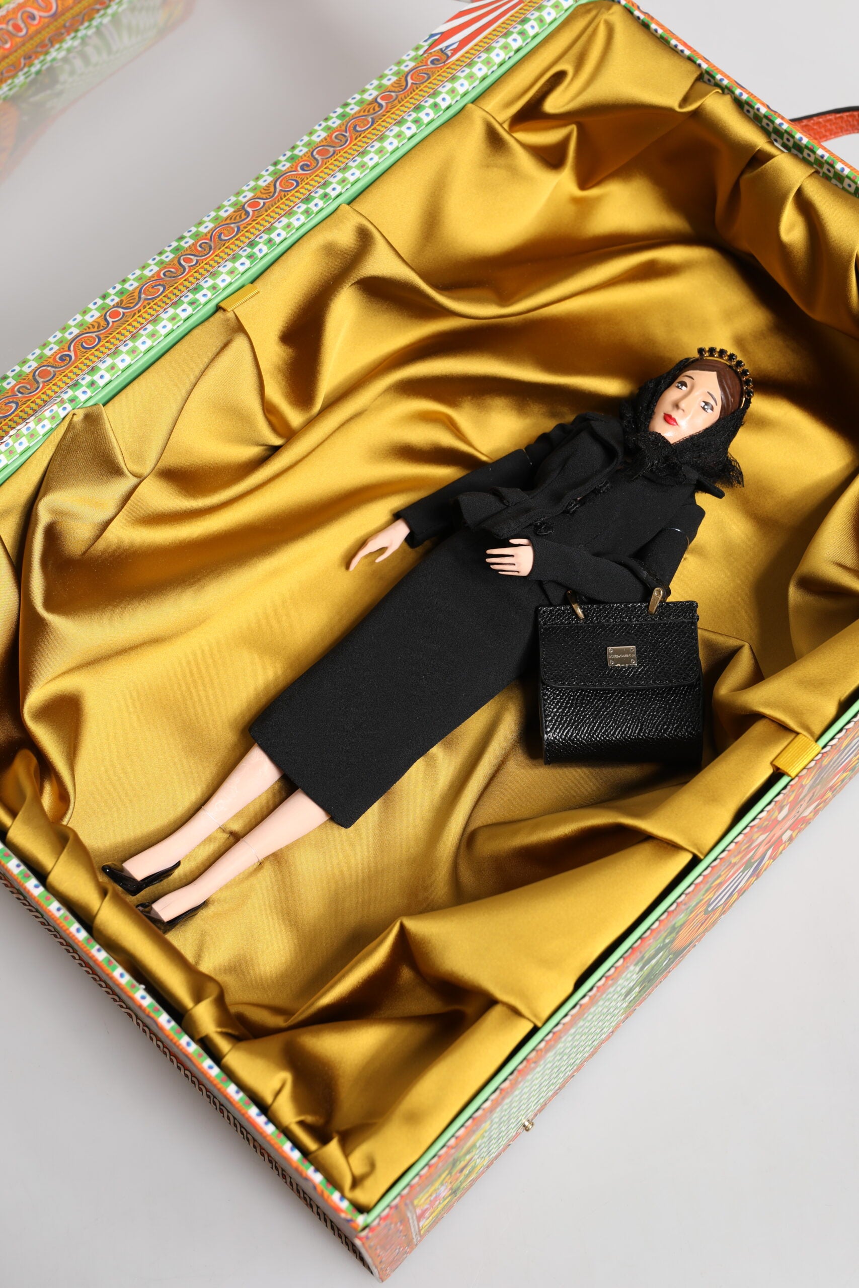 A porcelain doll wearing a black dress with leather details, part of the Dolce & Gabbana fashion collection