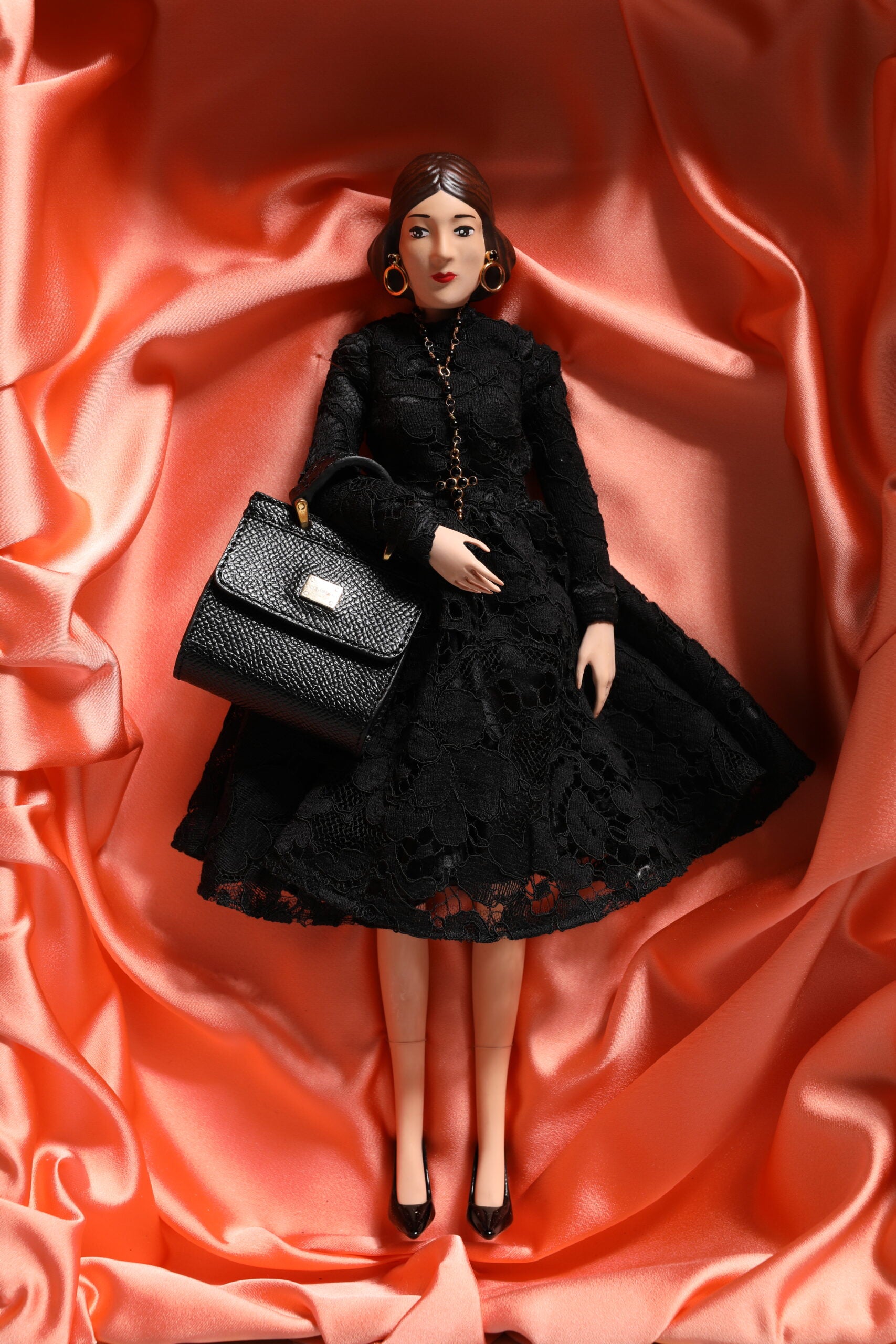 A porcelain doll wearing a black dress with lace and sequins, holding a black purse