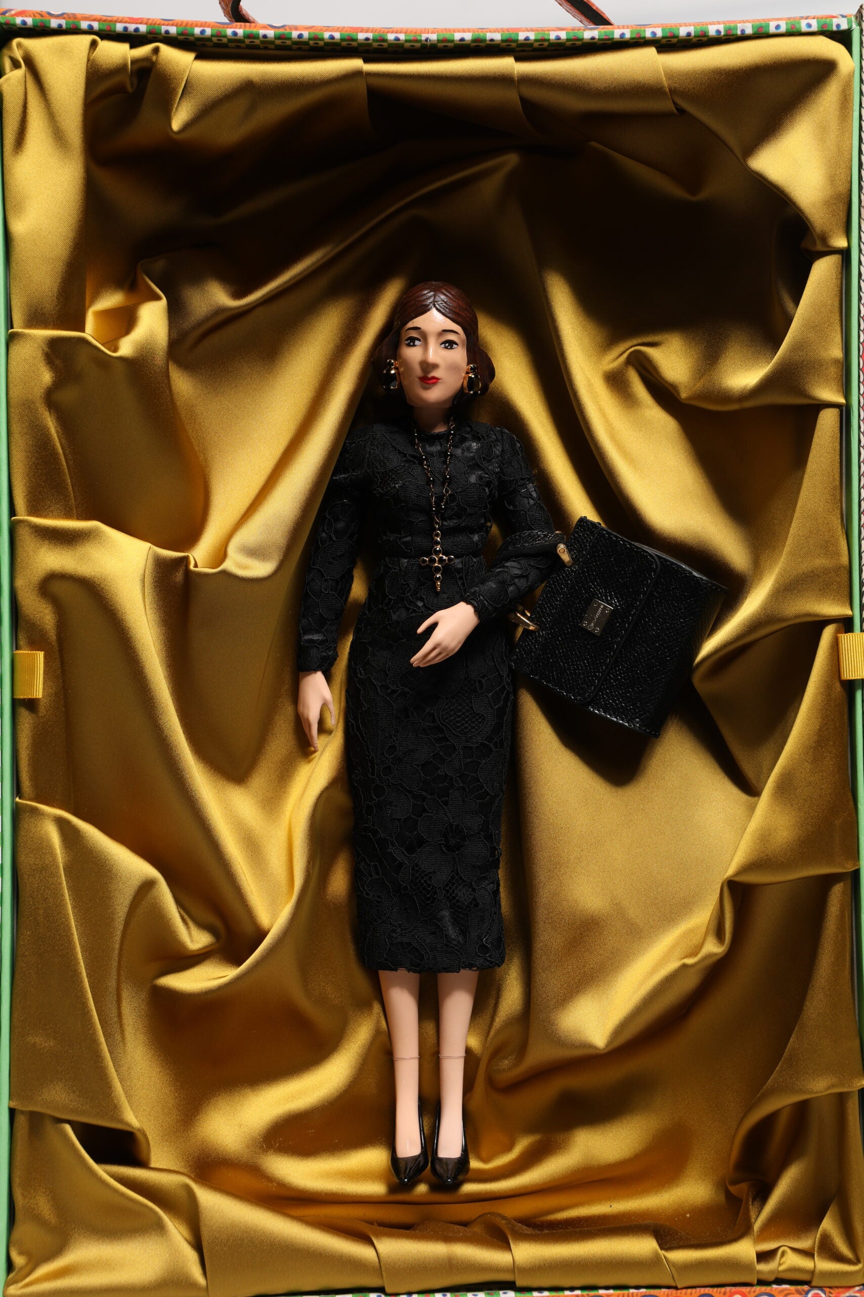 A porcelain doll wearing a black dress with gold accents, holding a black purse
