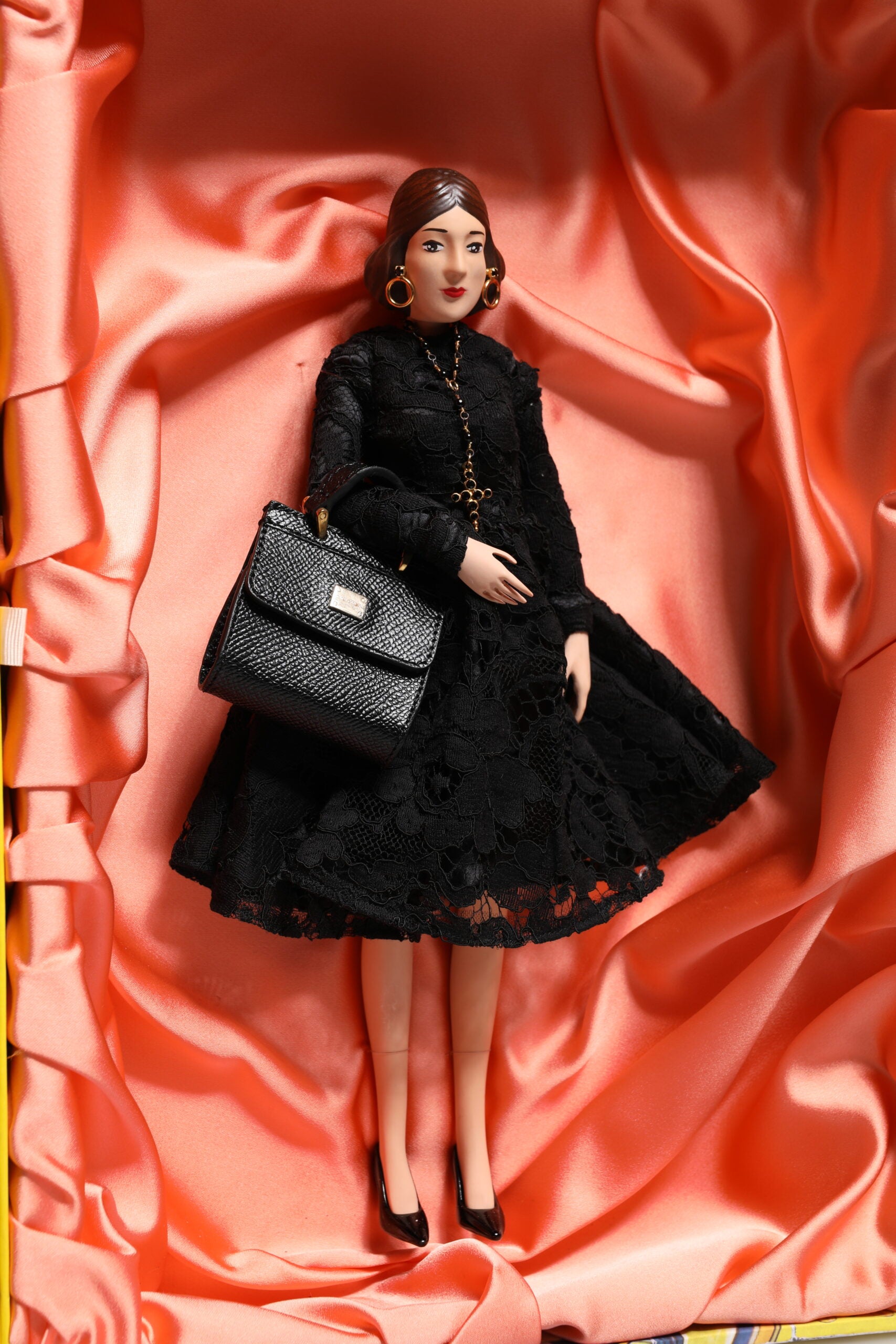 A porcelain doll wearing a black dress with lace and carrying a purse