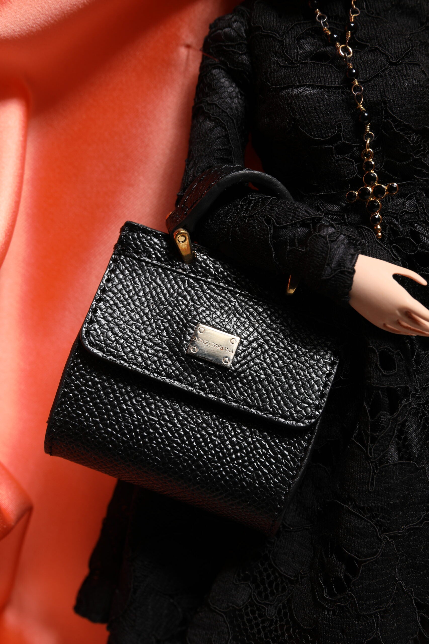 A black leather handbag with a gold clasp, held by a doll