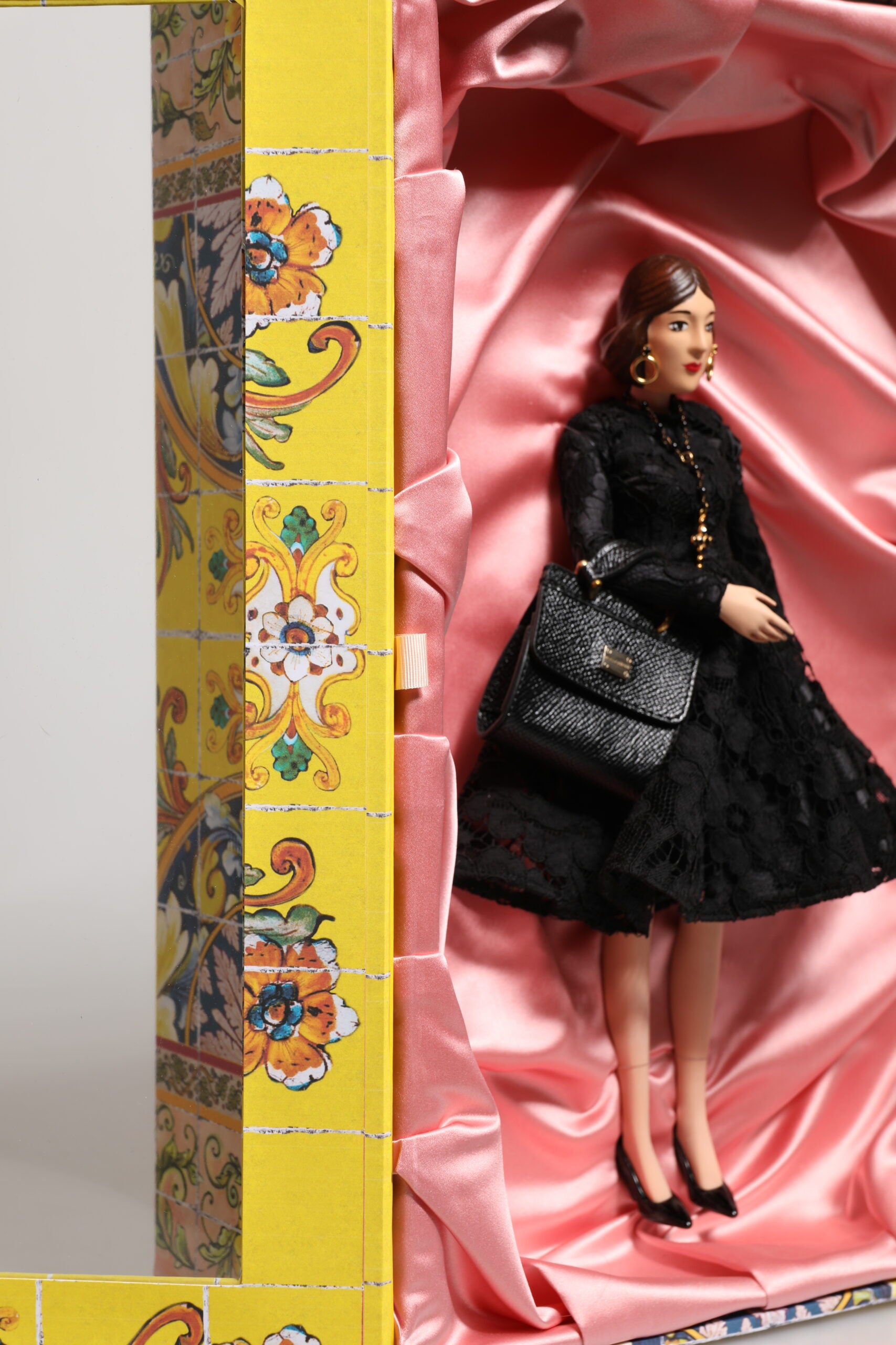 A porcelain doll wearing a black dress with gold accents, designed by Dolce & Gabbana