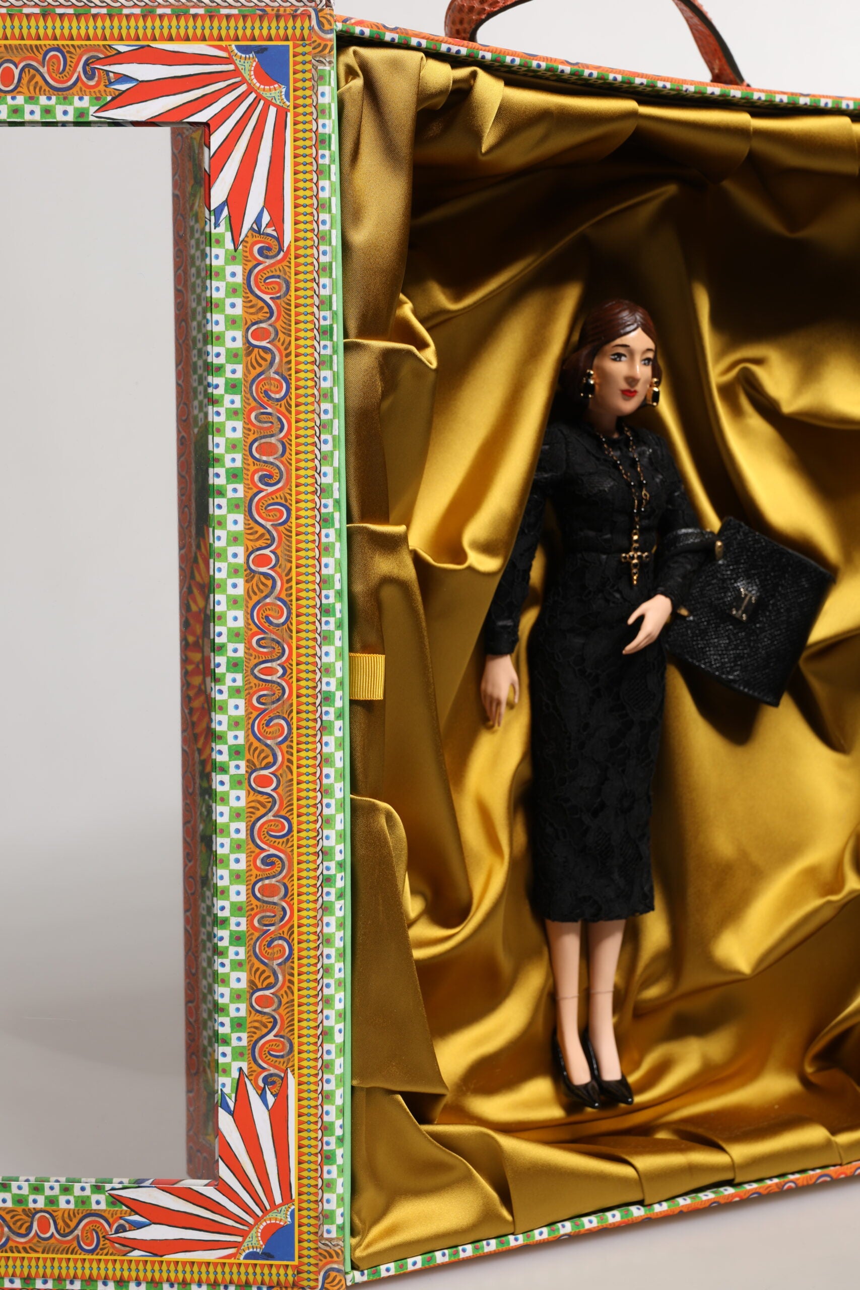A porcelain doll wearing a black dress with gold accents, designed by Dolce & Gabbana