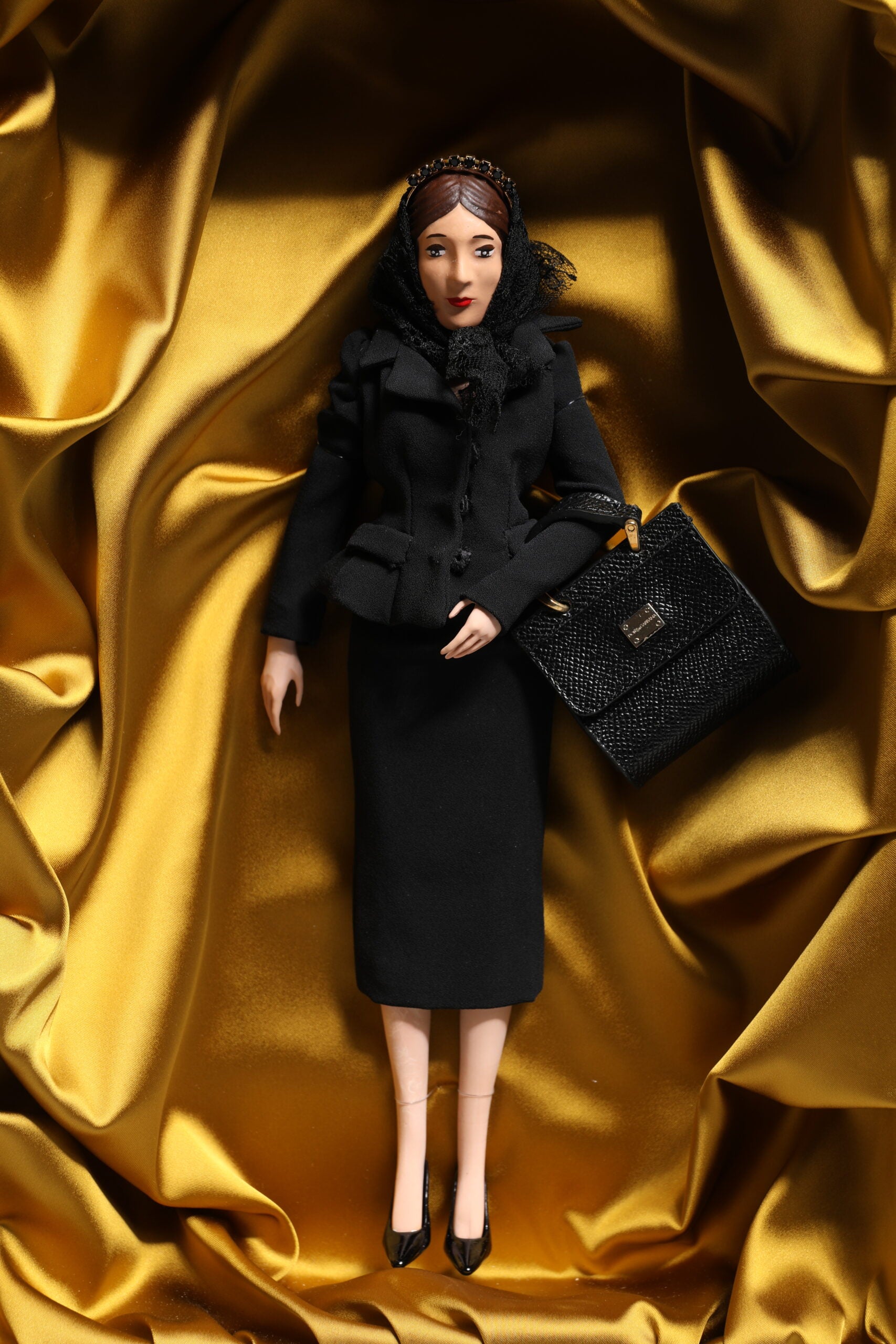 A porcelain doll wearing a black dress with lace and sequins, holding a purse
