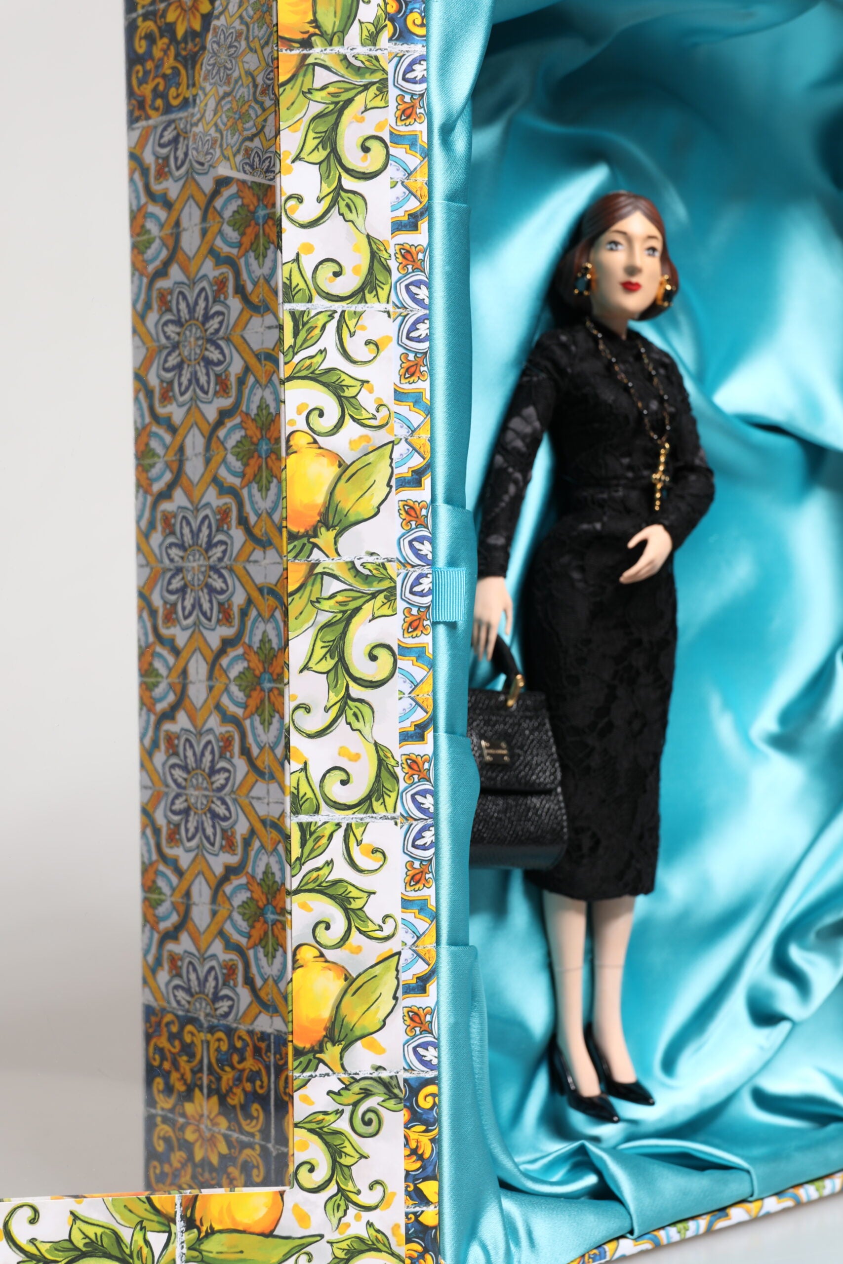 A porcelain fashion show doll wearing a black dress with gold accents
