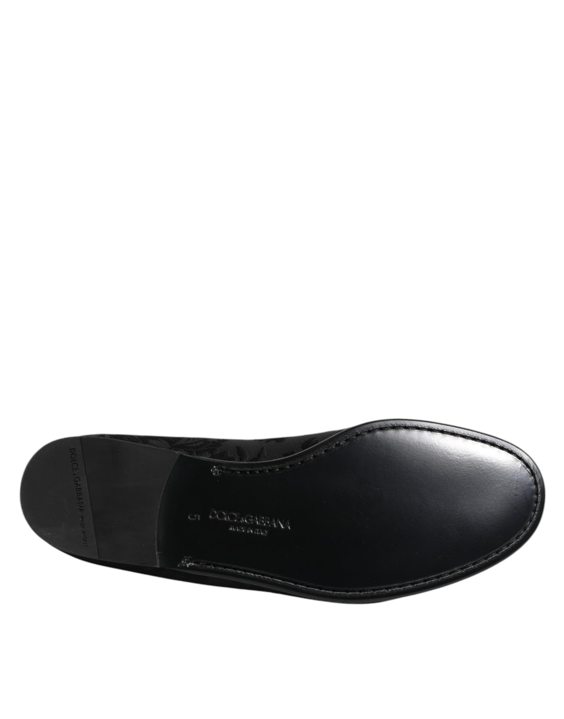 A single black loafer shoe with a floral brocade design, featuring a low heel and a strap across the top