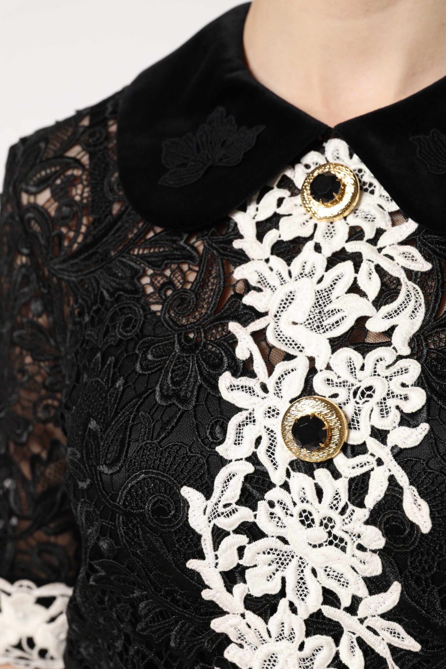 A black lace dress with floral embellishments and a gold button detail on the front