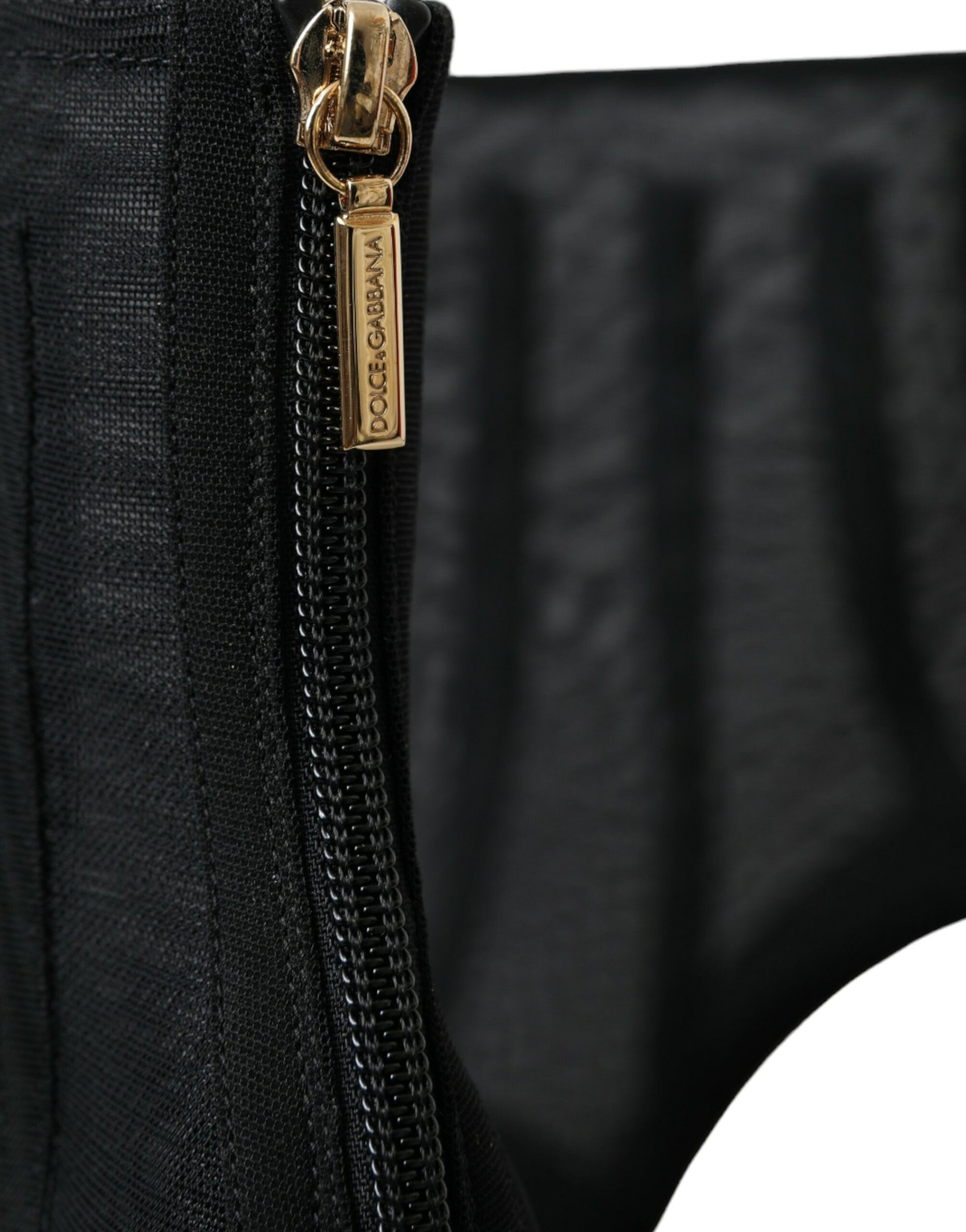 Zipper on black fabric with a gold chain and tag attached to it