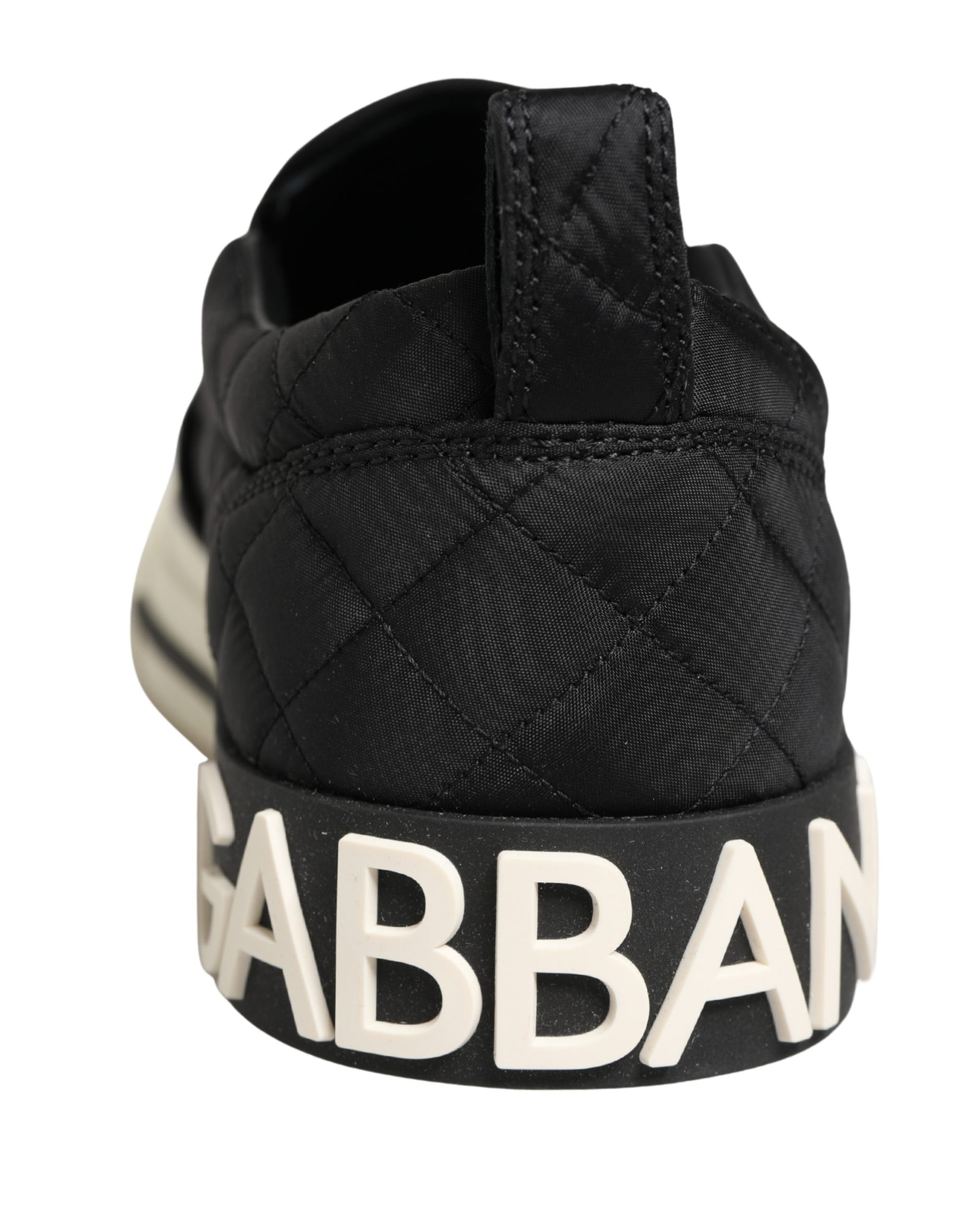 A pair of black quilted slip-on shoes with the word "GABBANA" in white letters