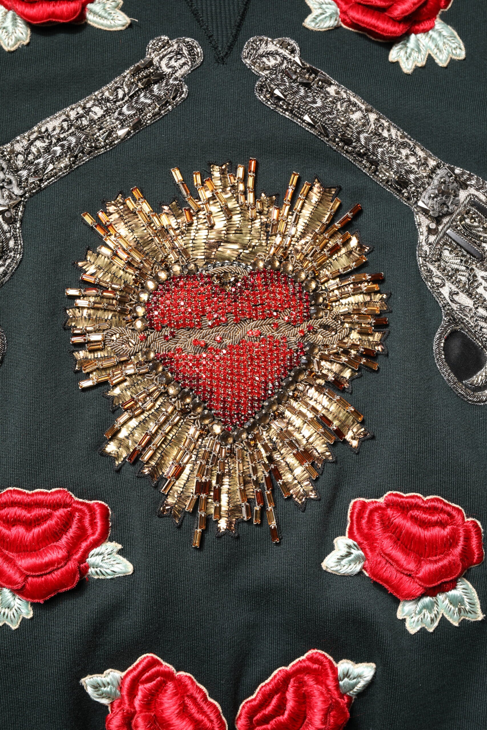 Decorative embroidery on a dark fabric featuring a heart design with red roses and gold accents