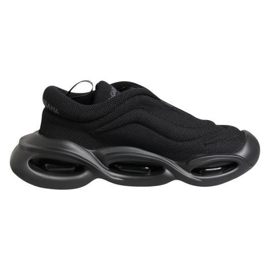 A pair of black slip-on shoes with a low top and wave design on the sole
