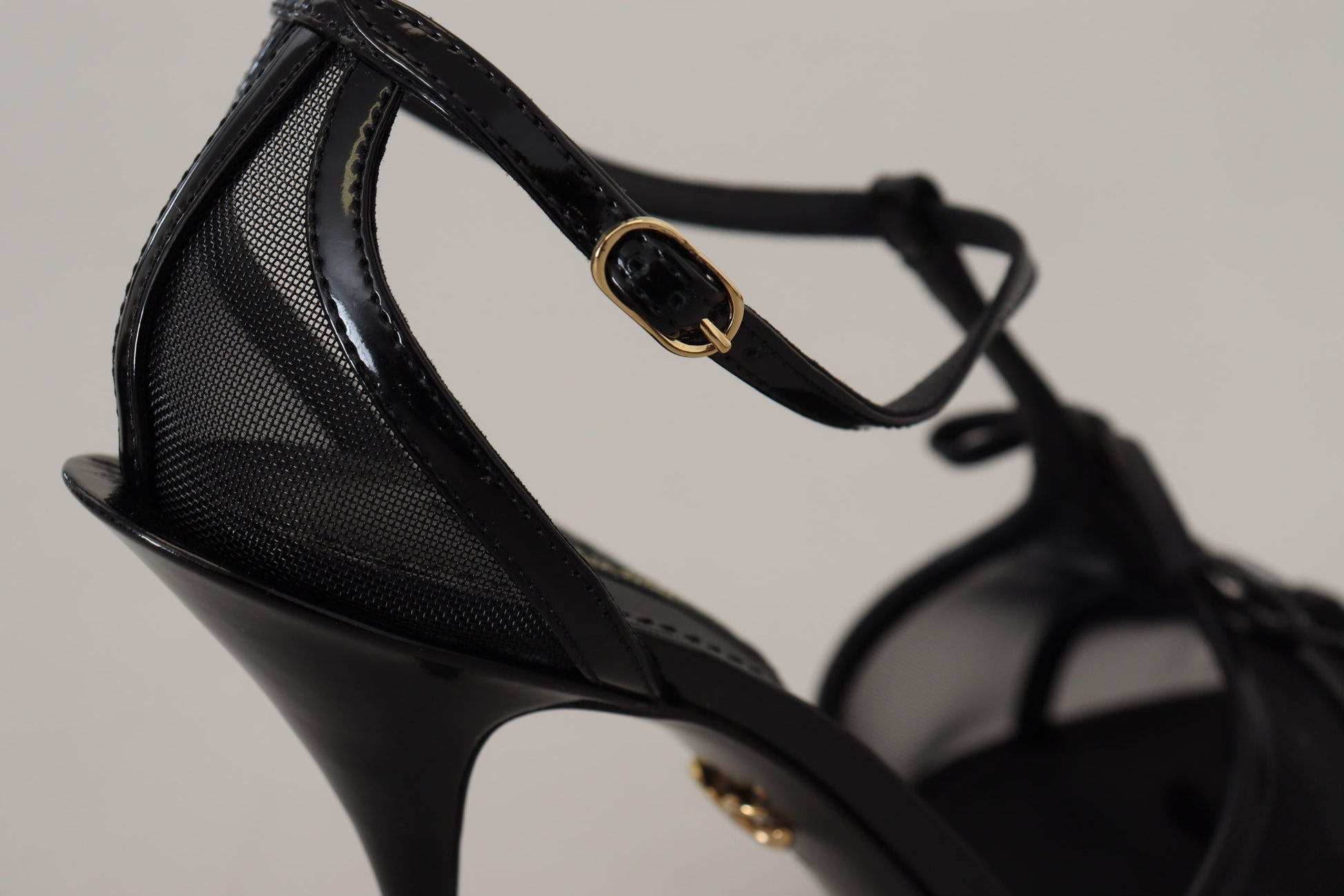 Black high heel shoe with a stiletto heel and gold hardware