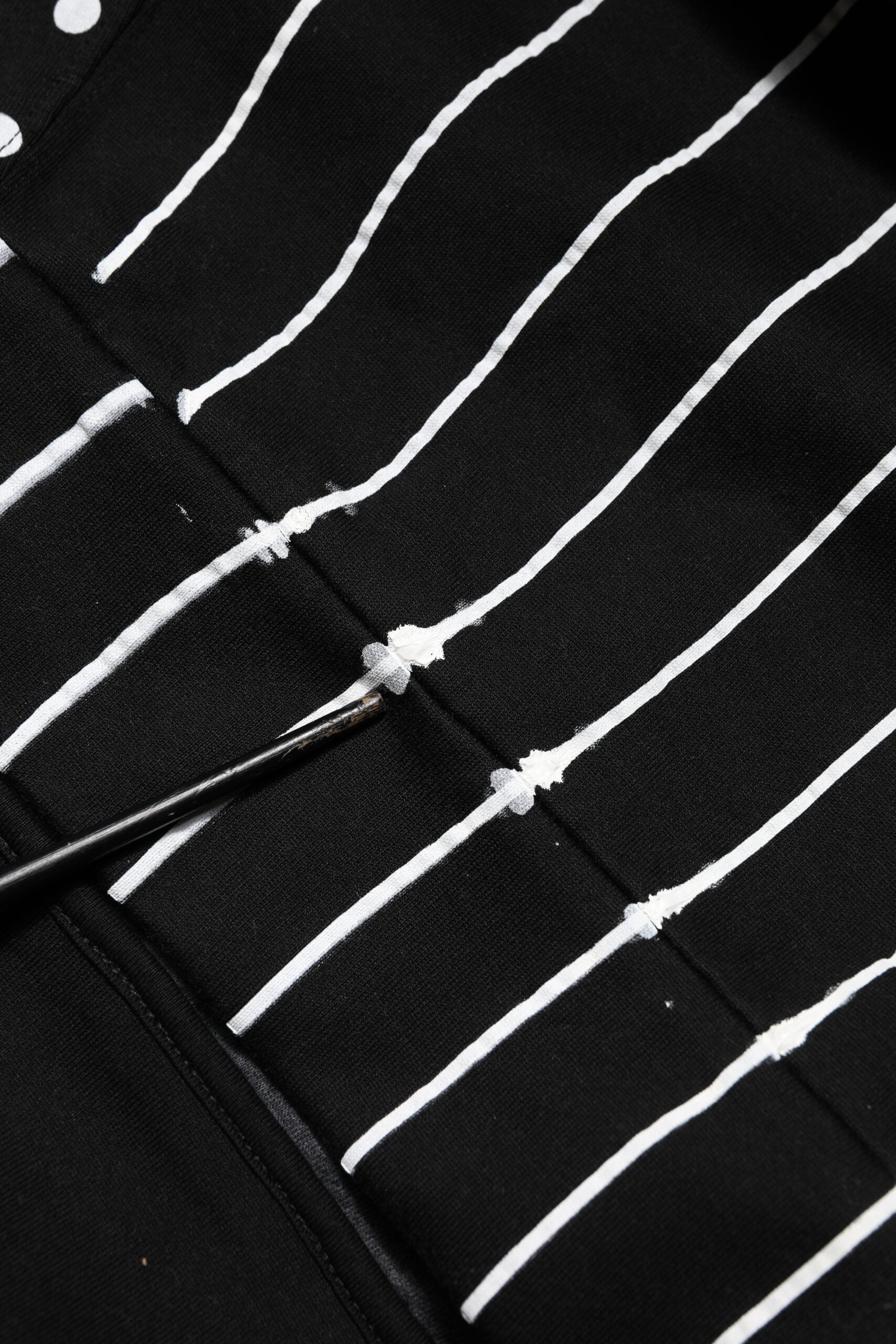 Black fabric with white lines and a metal needle threaded through it