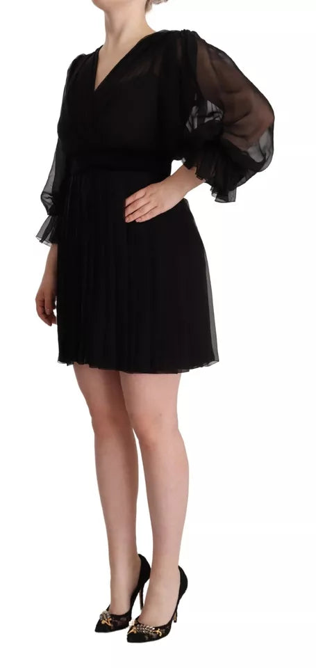 A black dress with long sleeves and a V-neck. It features ruffled details on the shoulders and is designed in