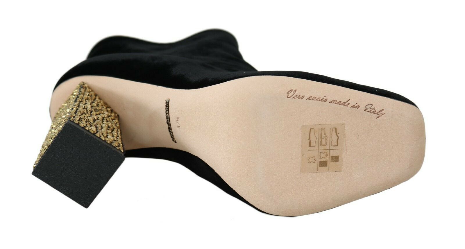 A single shoe with a black velvet upper and a gold buckle on the side. There is a label on the tongue of the shoe that re