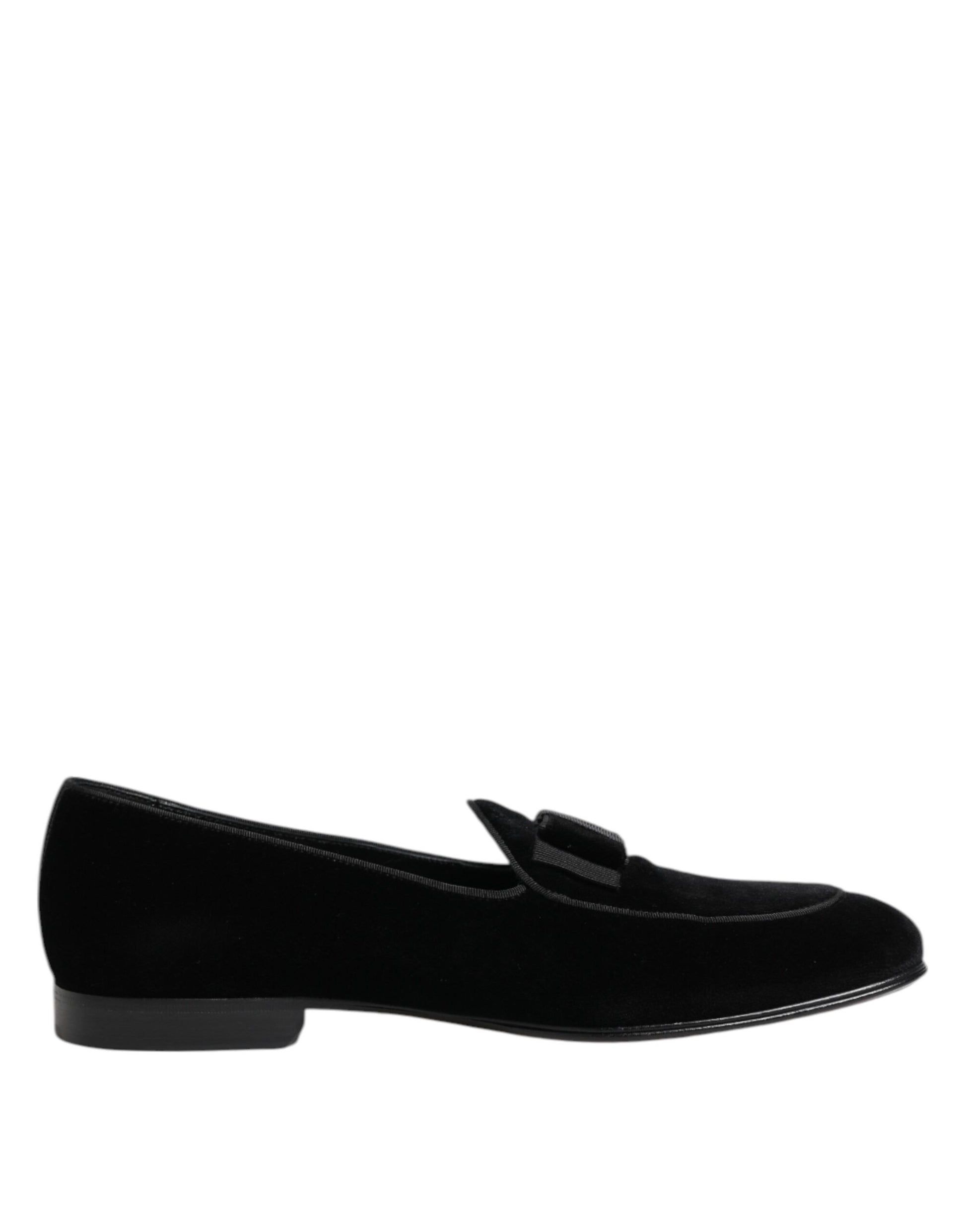 A pair of black velvet loafers with a shiny finish, featuring a low heel and a bow on the side