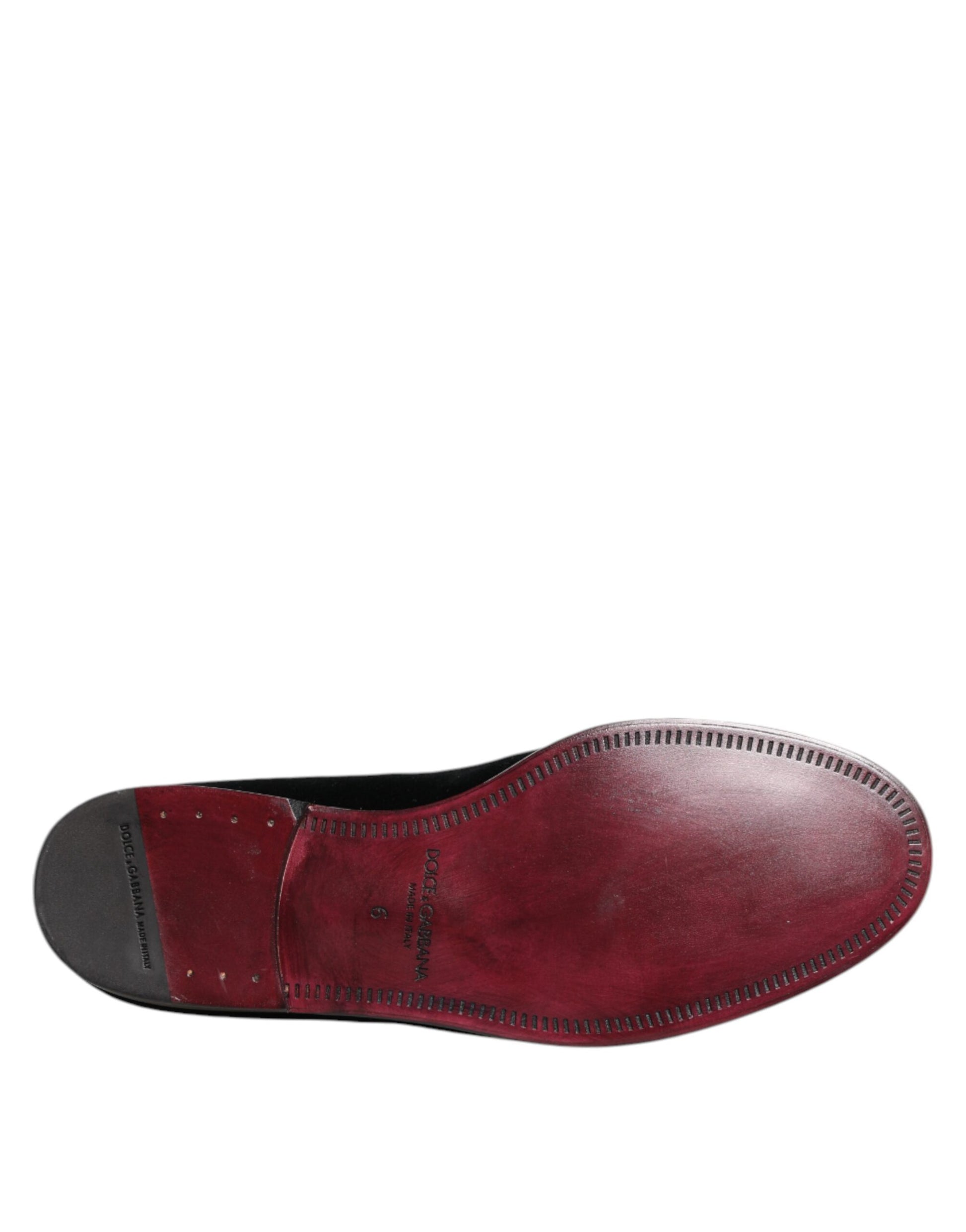 A single black velvet loafer shoe with a red sole, featuring stitched details and a classic design