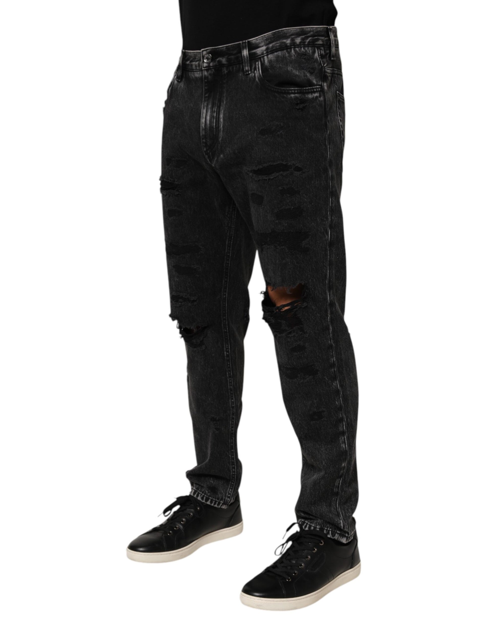 Man wearing black denim jeans with distressed areas and a pair of black sneakers