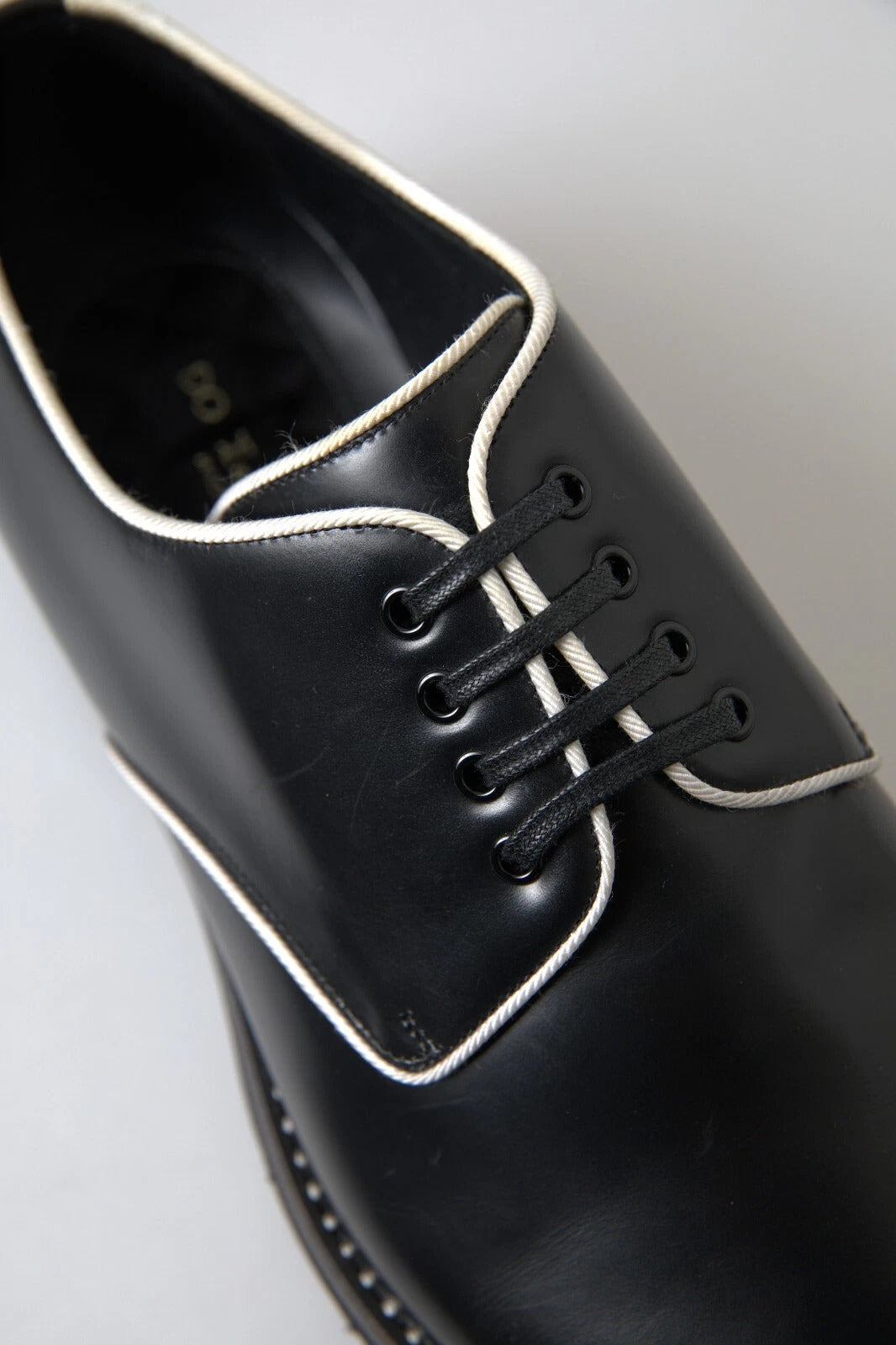 A pair of black leather dress shoes with white laces and a bow tie design on the vamp