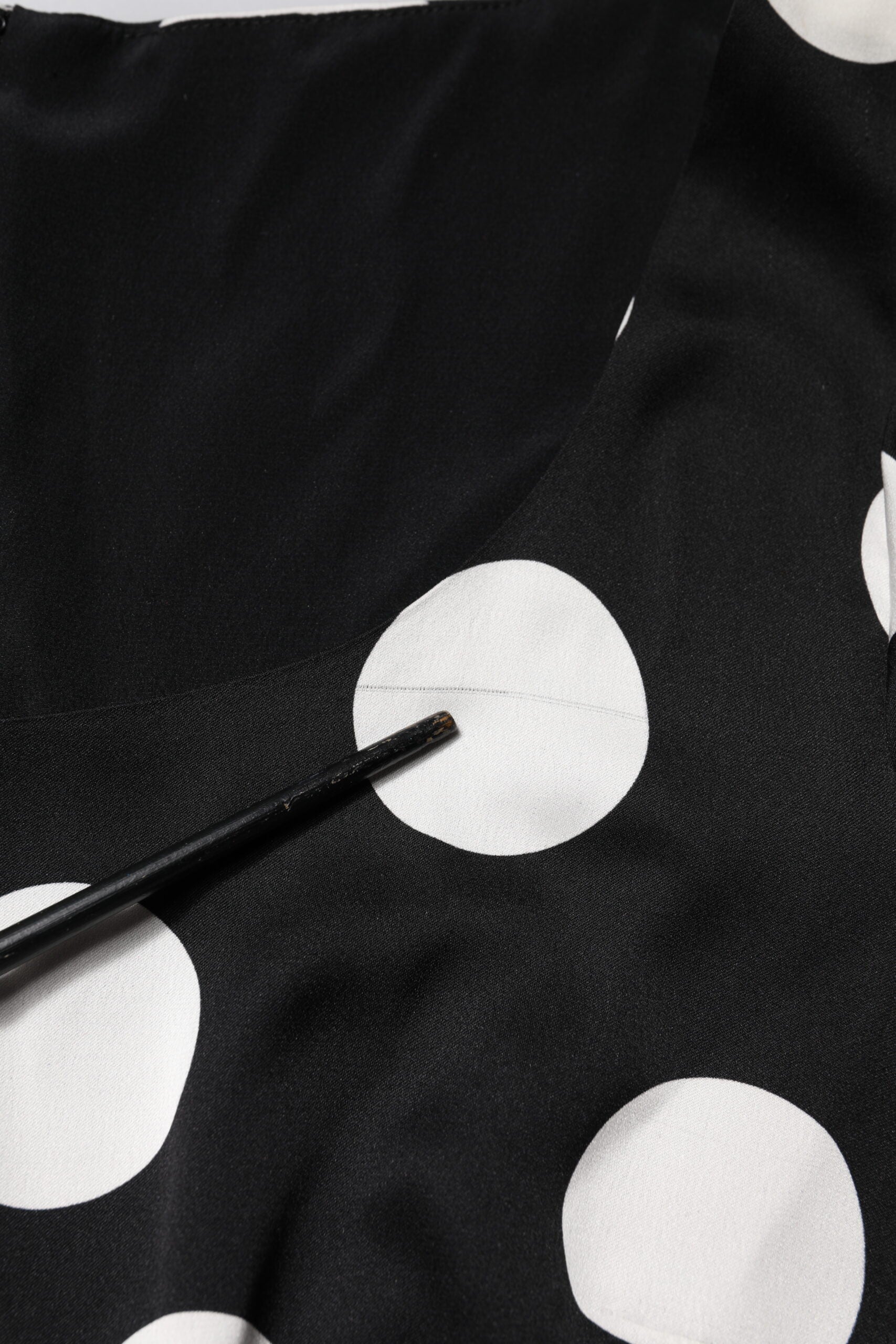 A black midi dress with white polka dots, featuring a sheath silhouette