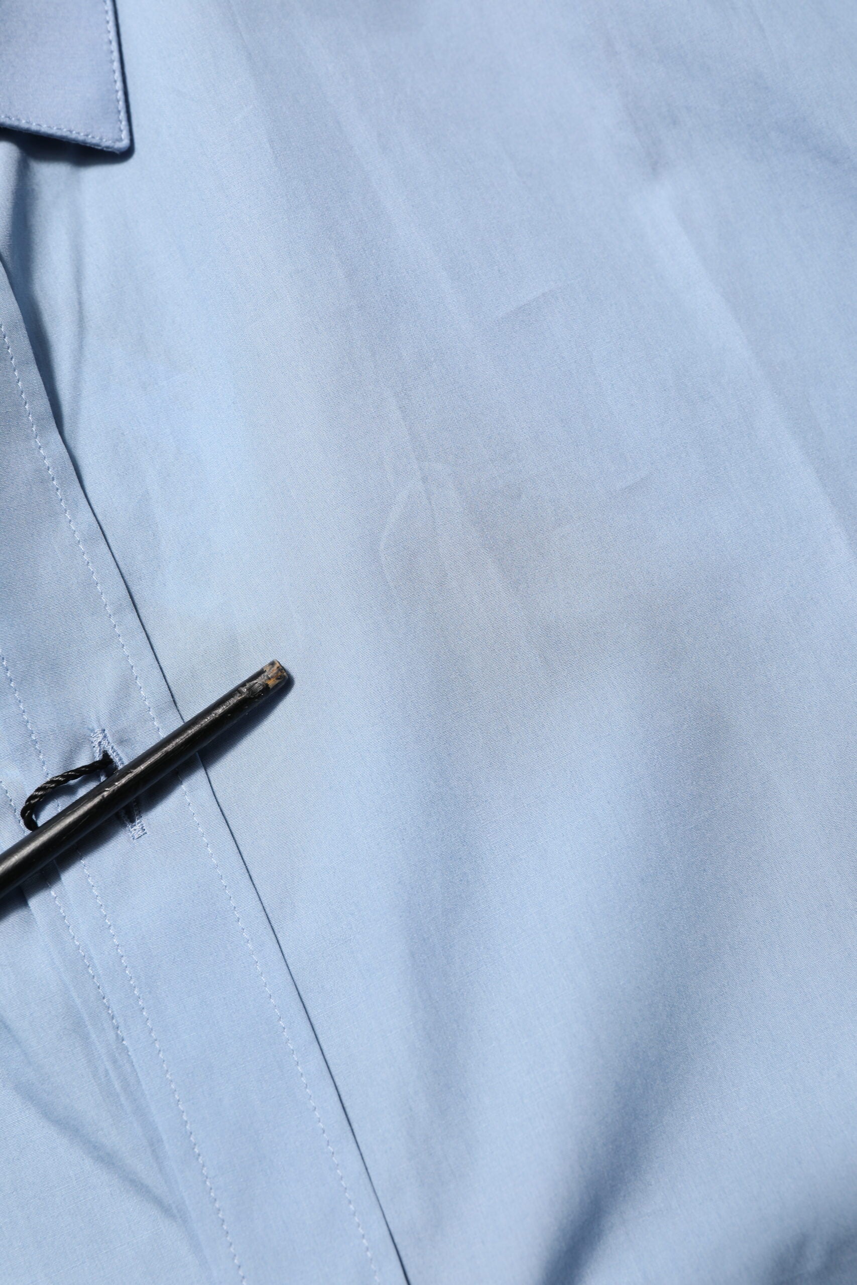 A blue cotton collared dress shirt with a gold pin on the left side