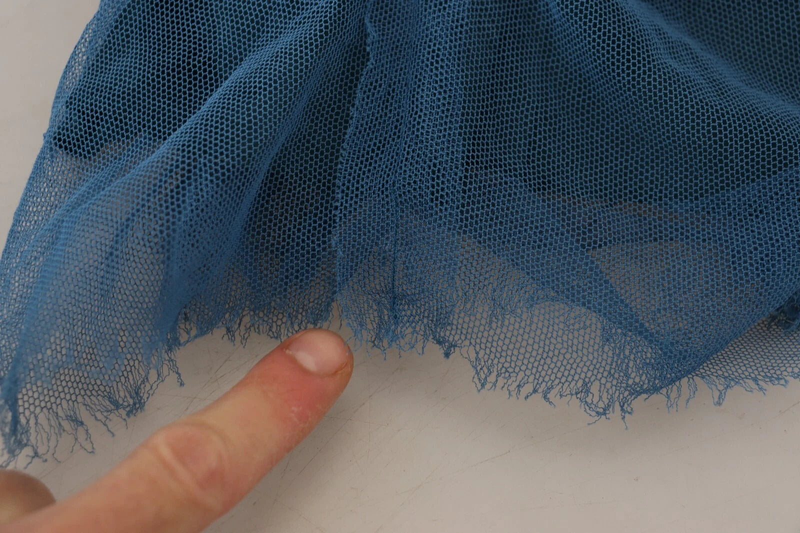 A blue mesh trim ruched tulle sheath dress with a finger pointing to the fabric