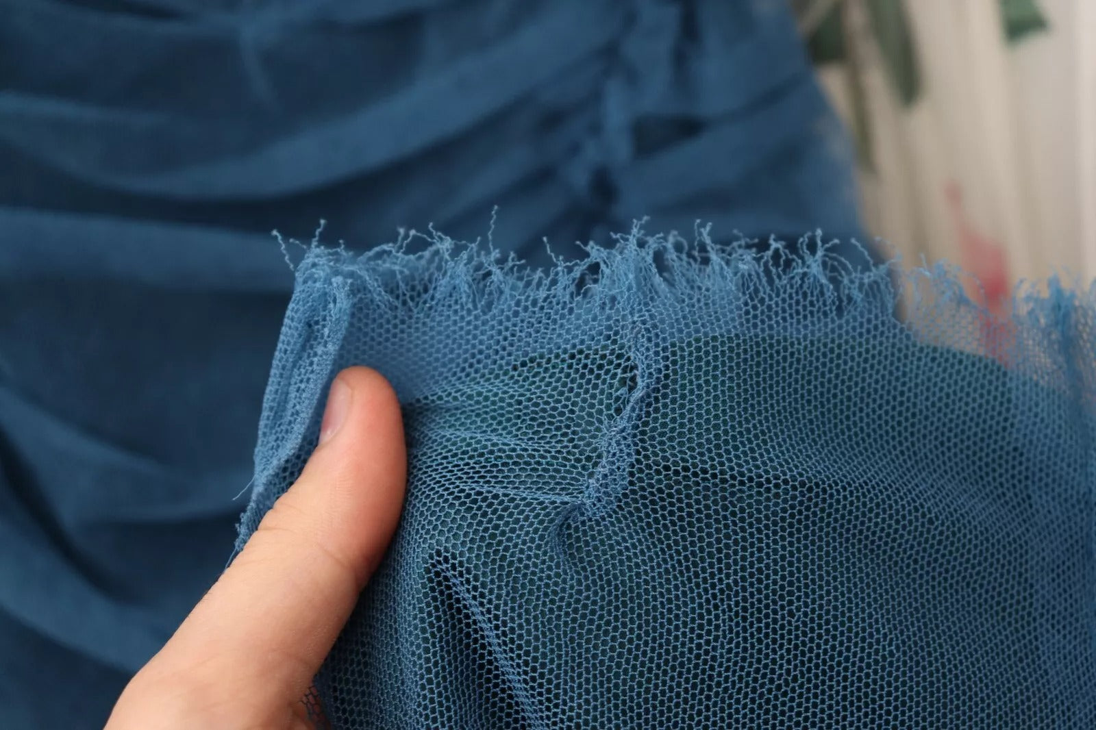 A person's hand holding a blue mesh trim ruched tulle sheath dress