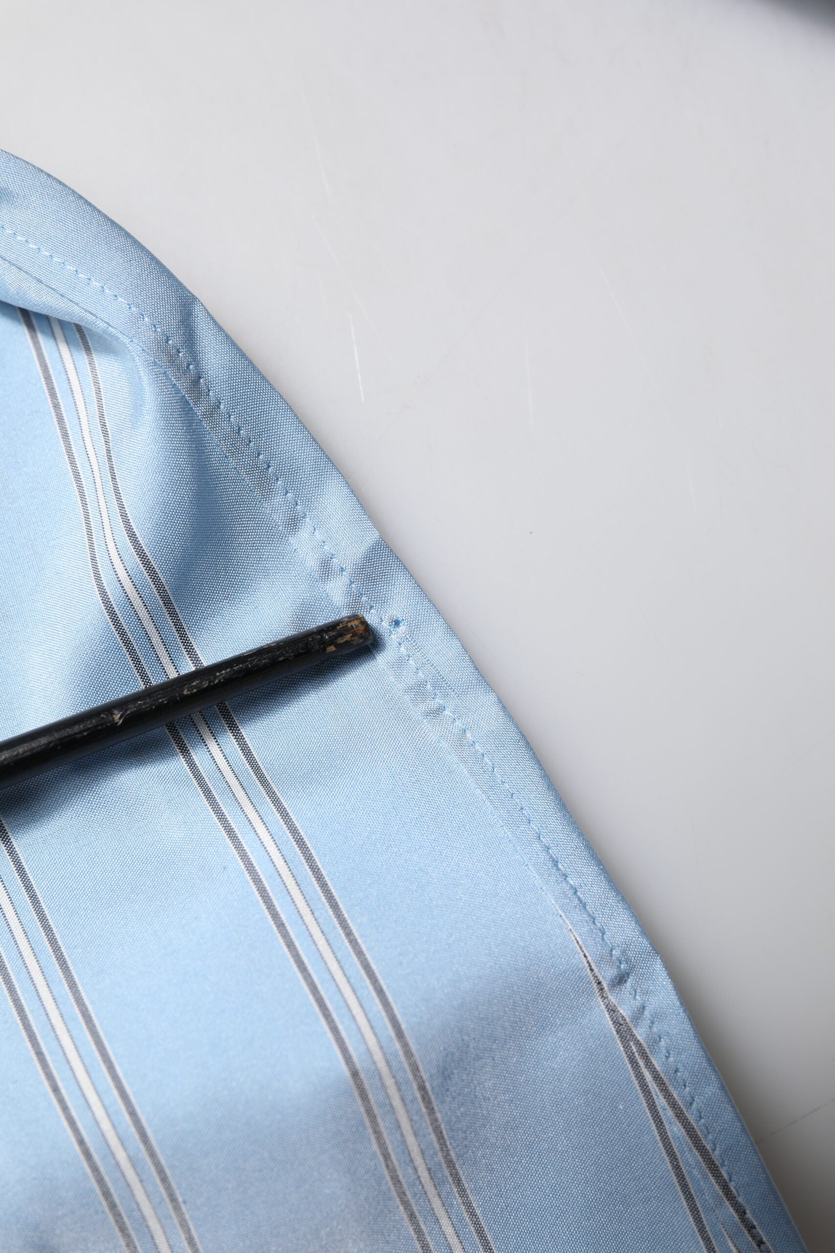A blue striped dress shirt with a black tie pin