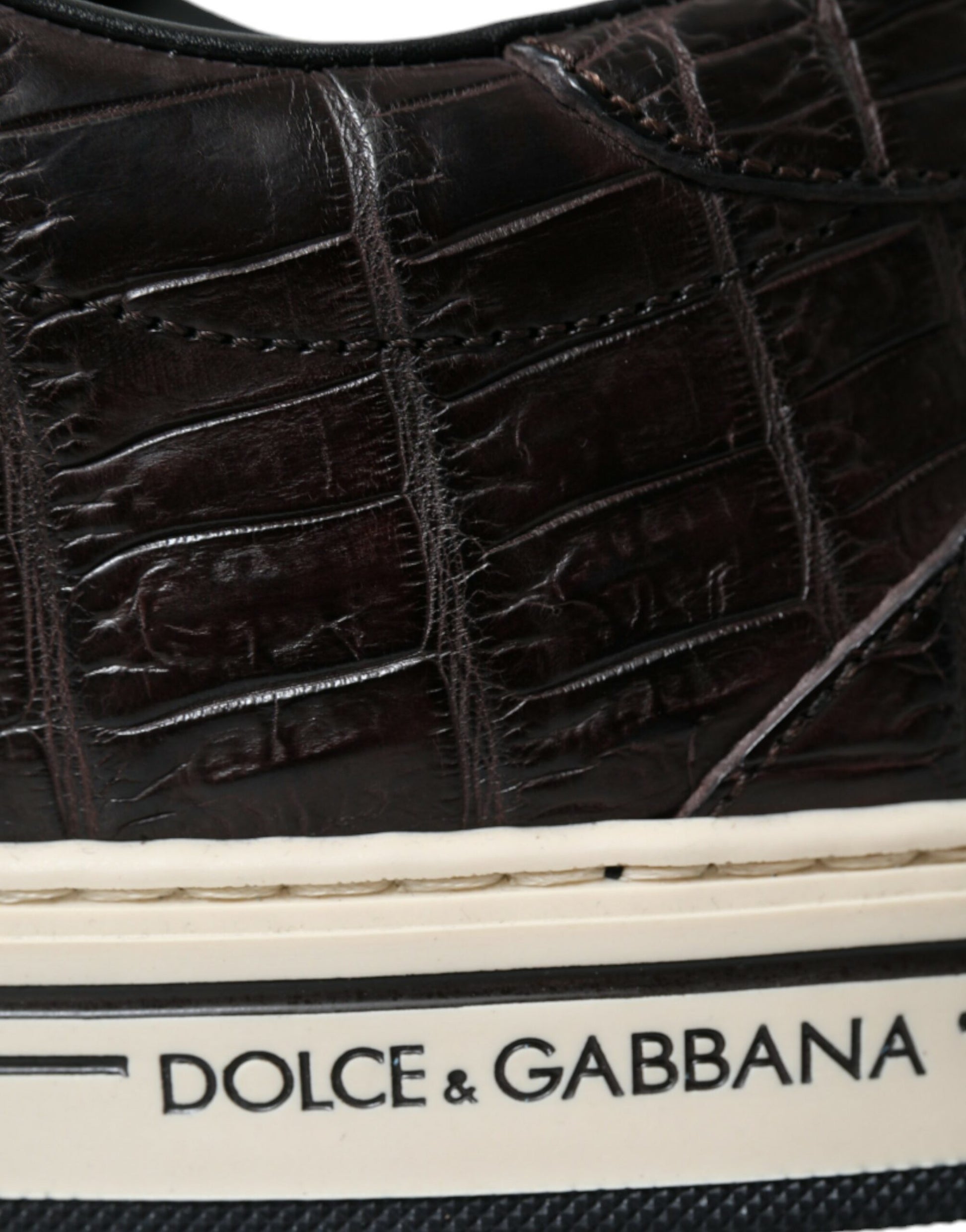 A pair of brown crocodile skin sneakers with white soles and laces, featuring the brand names "Dolce & Gabbana" on the side