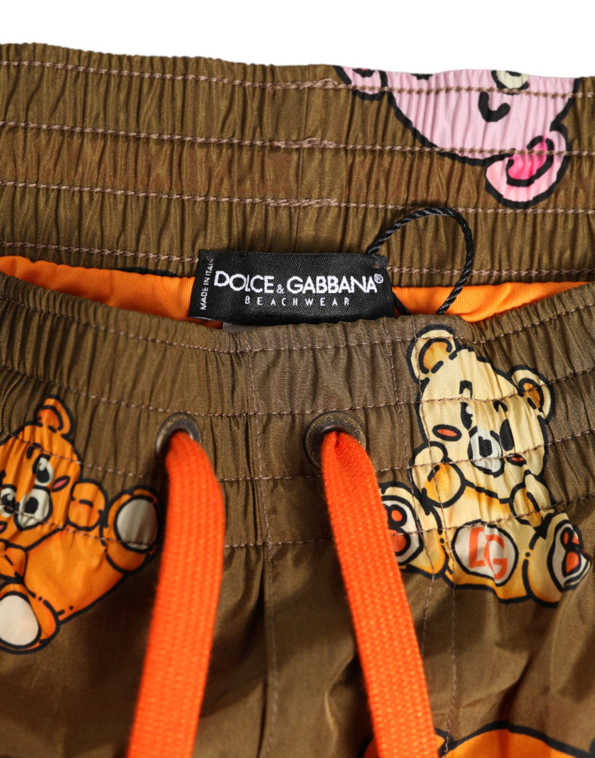 A pair of brown swim trunks with a teddy bear pattern and orange trim