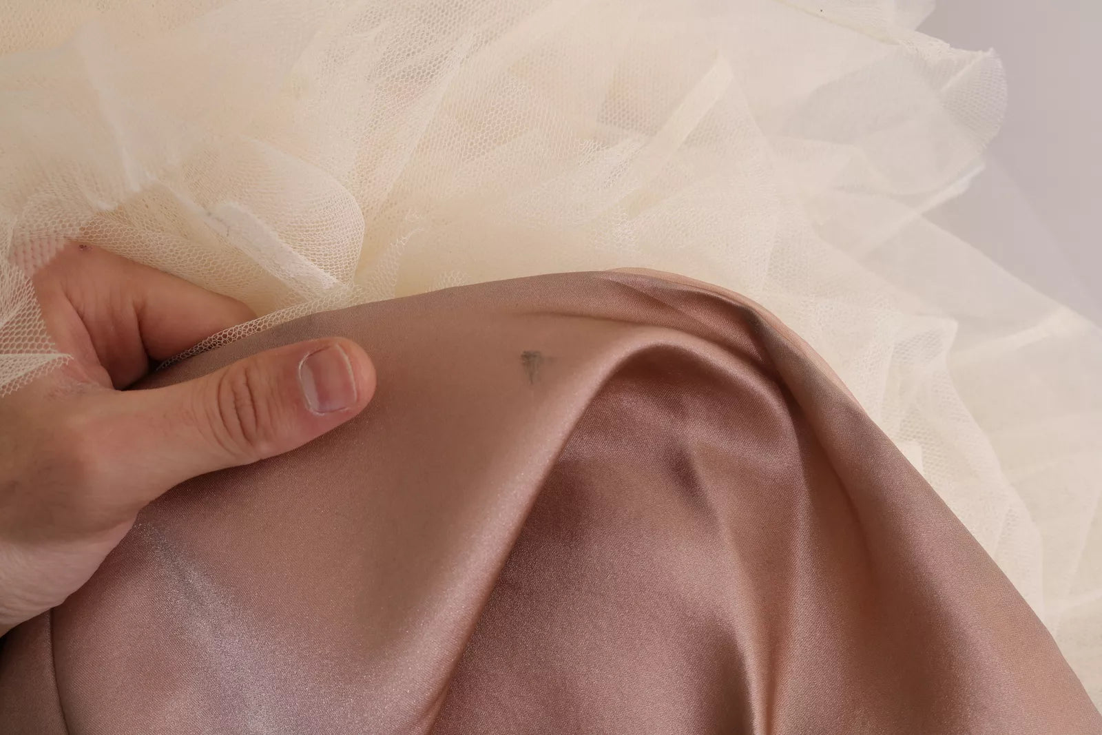 A person's hand touching a pink silk chiffon dress with a crystal embellishment