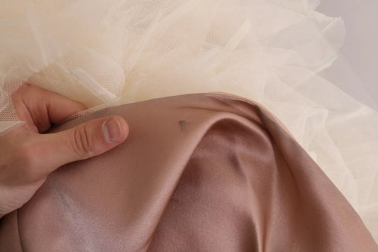 A person's hand touching a pink silk chiffon dress with a crystal embellishment