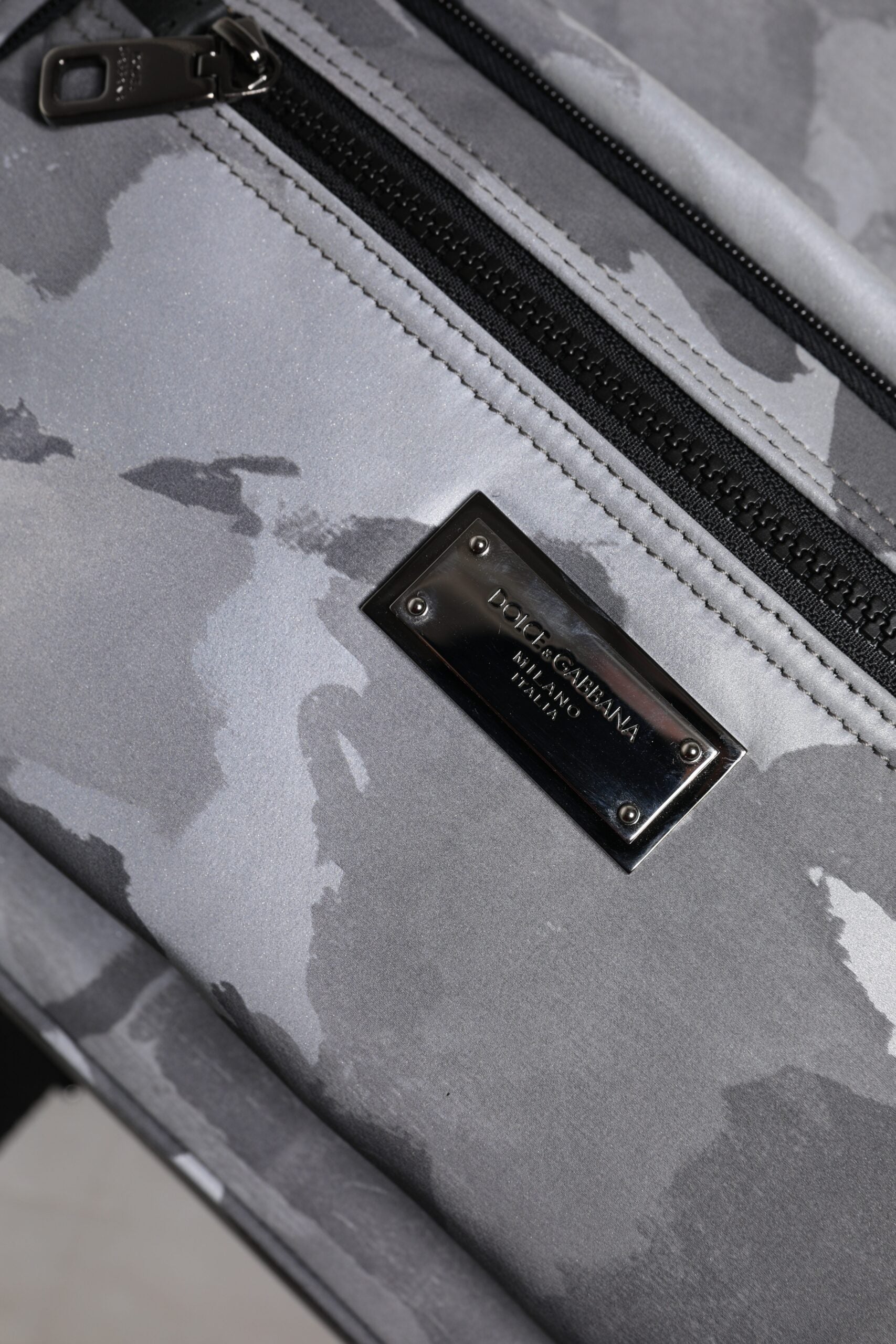 Grey camouflage suitcase with black zipper and metal plaque on front