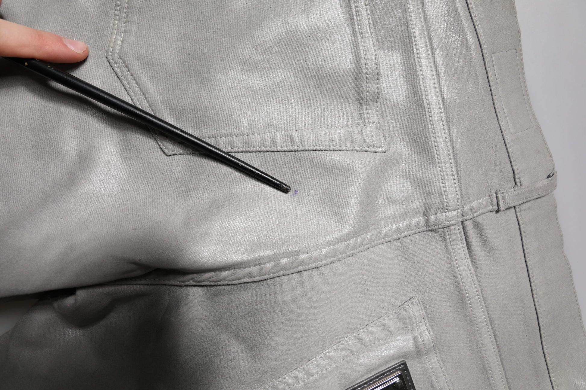 Hand holding black pen over pocket of gray pants