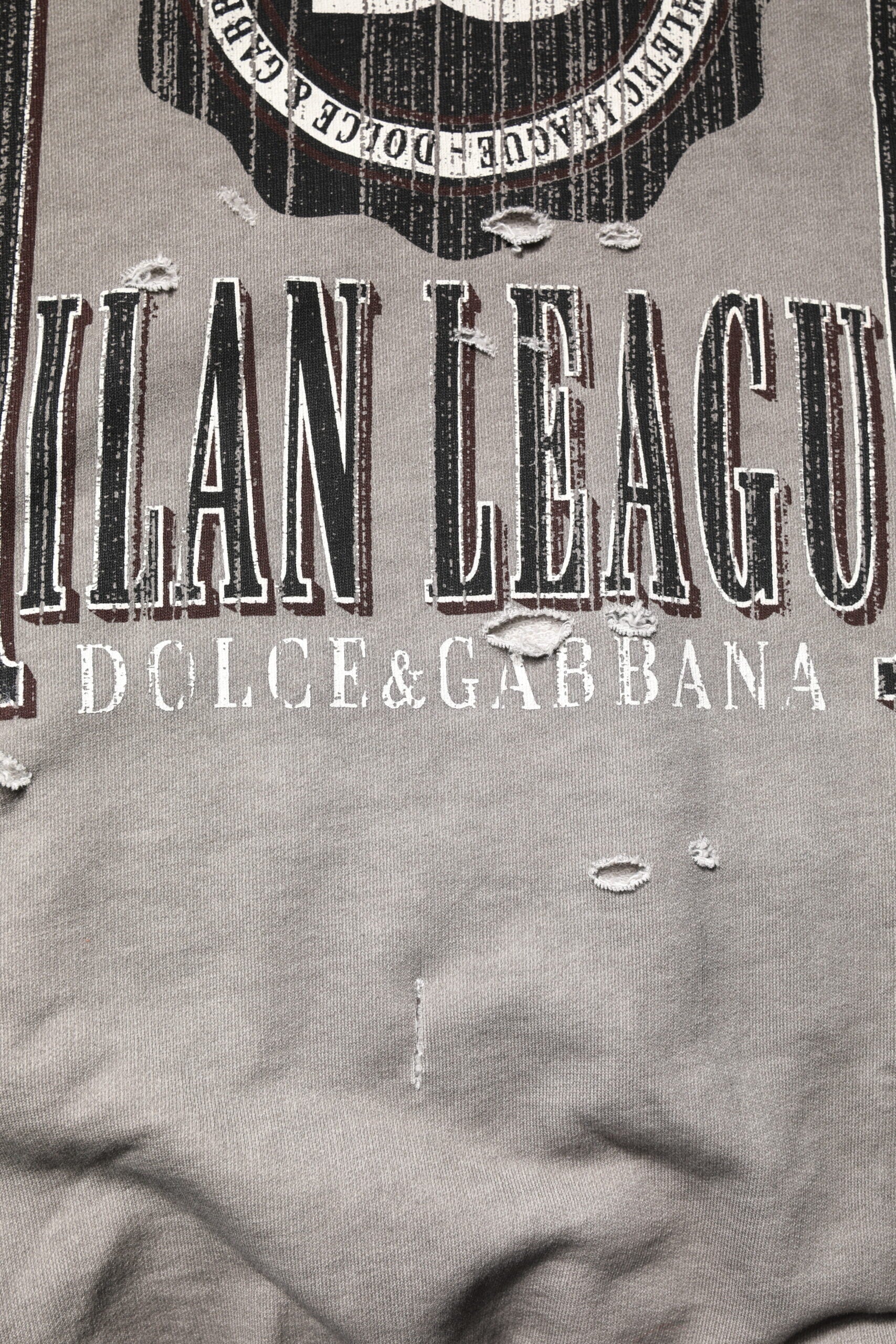 A close-up of a fabric item with printed text on it. The visible text includes "VLAN LEAGUE," "DOLCE & GABBAN