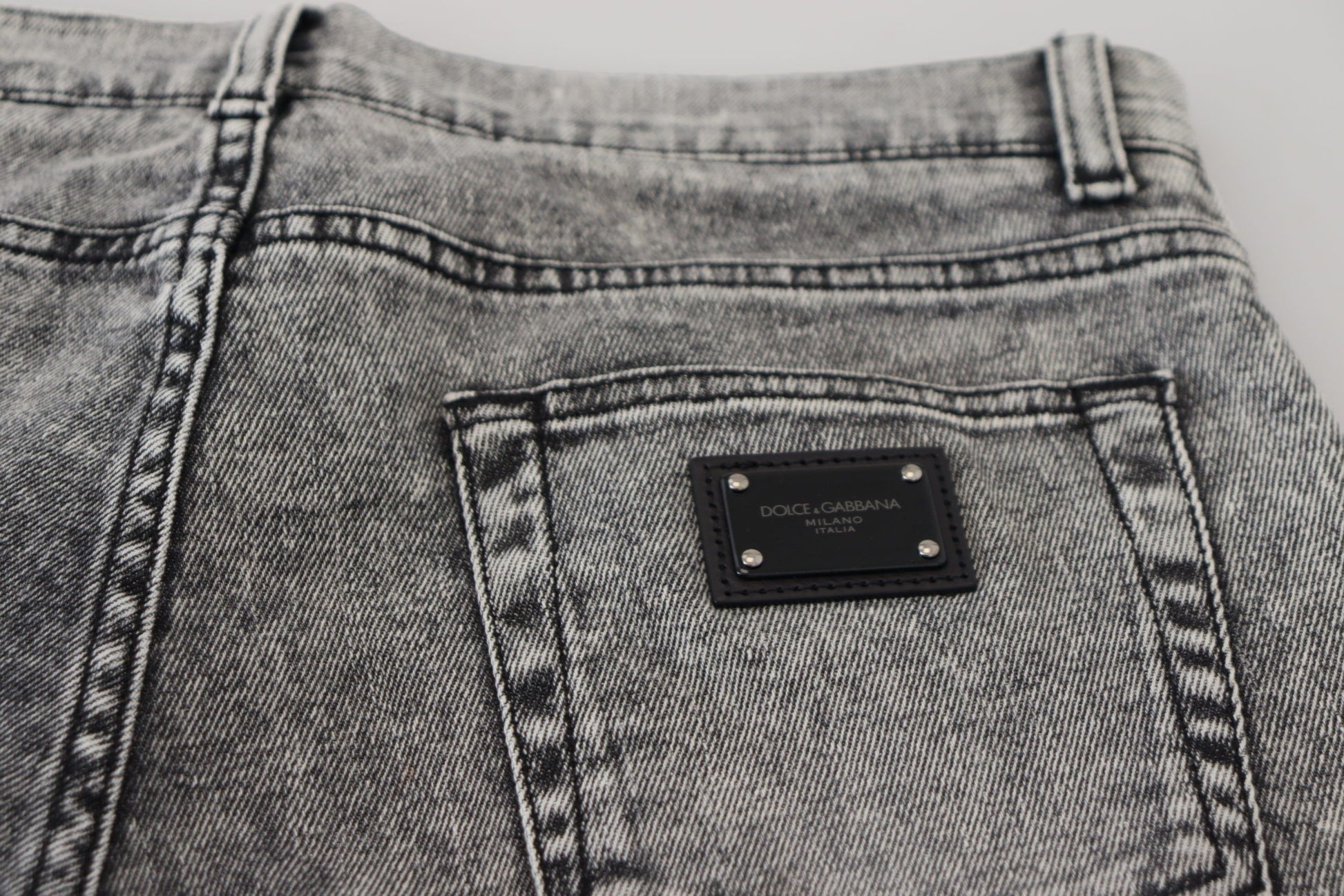 Pair of light blue denim jeans with a small rectangular metal plaque on the right side of the waistband