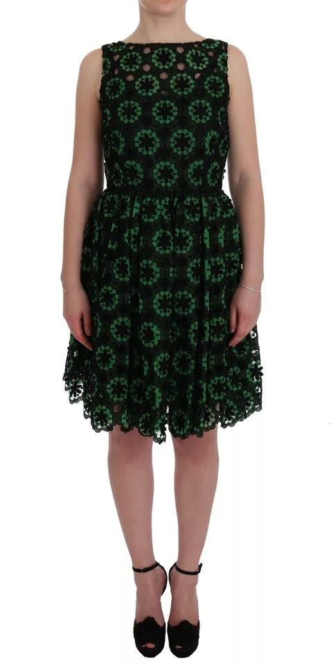A woman wearing a green dress with floral patterns and ricamo detailing. The dress has an A-line silhouette a
