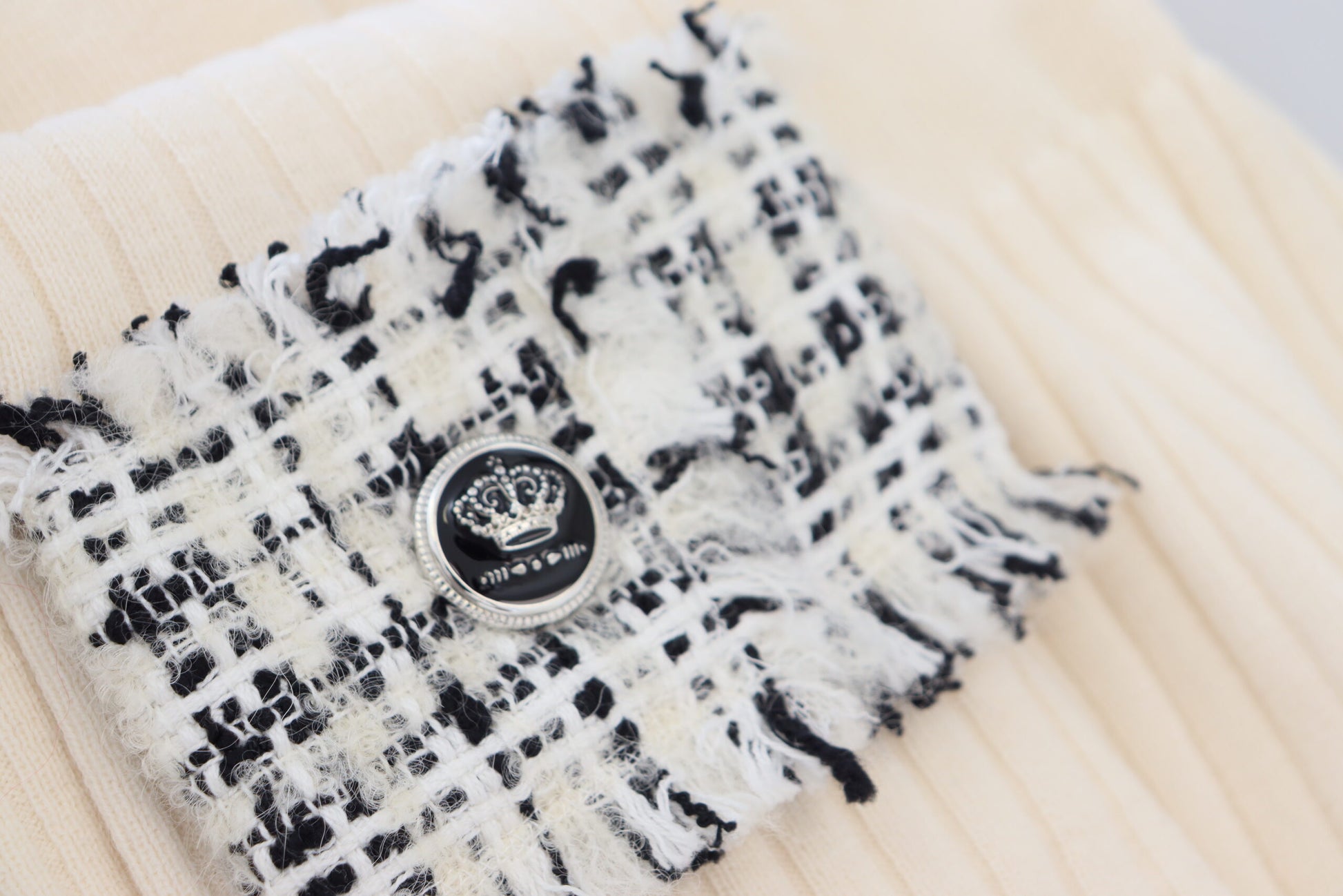 Black and white argyle patterned scarf with a button closure featuring a crown emblem