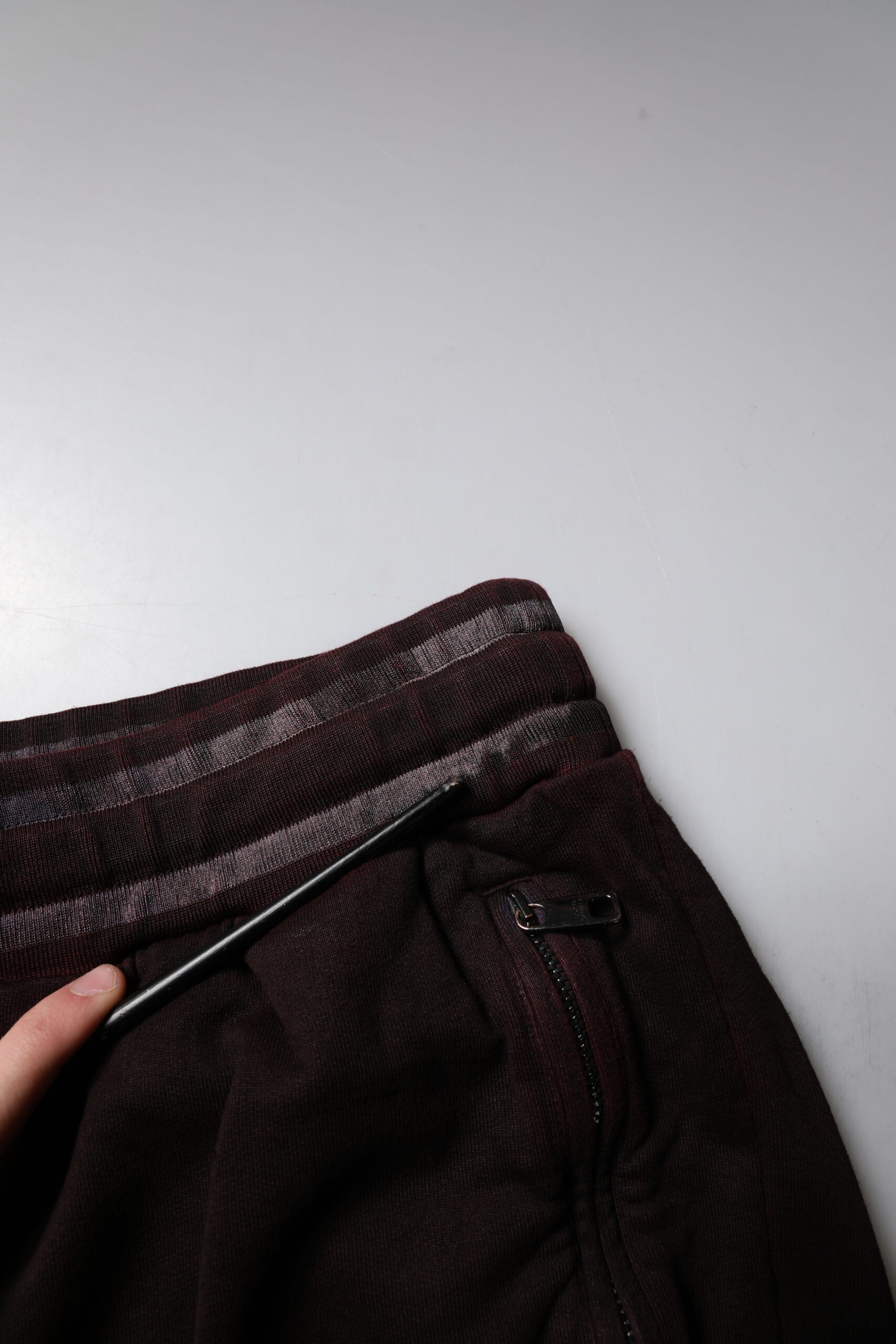 Hand holding a black pen over a pair of dark pants on a white surface